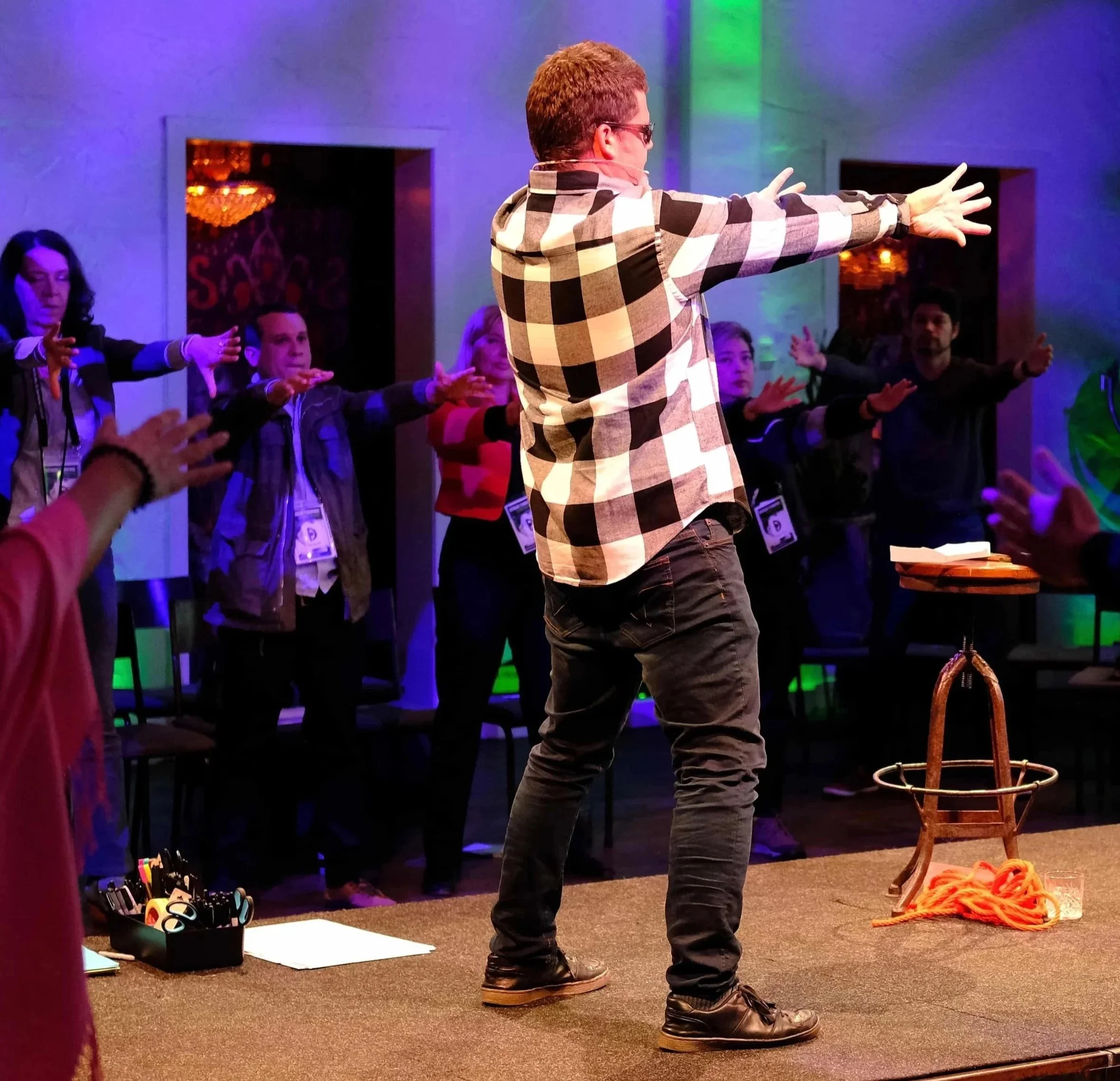 Man leading a group in stretching or yoga exercises in a dimly lit room with colorful lighting.