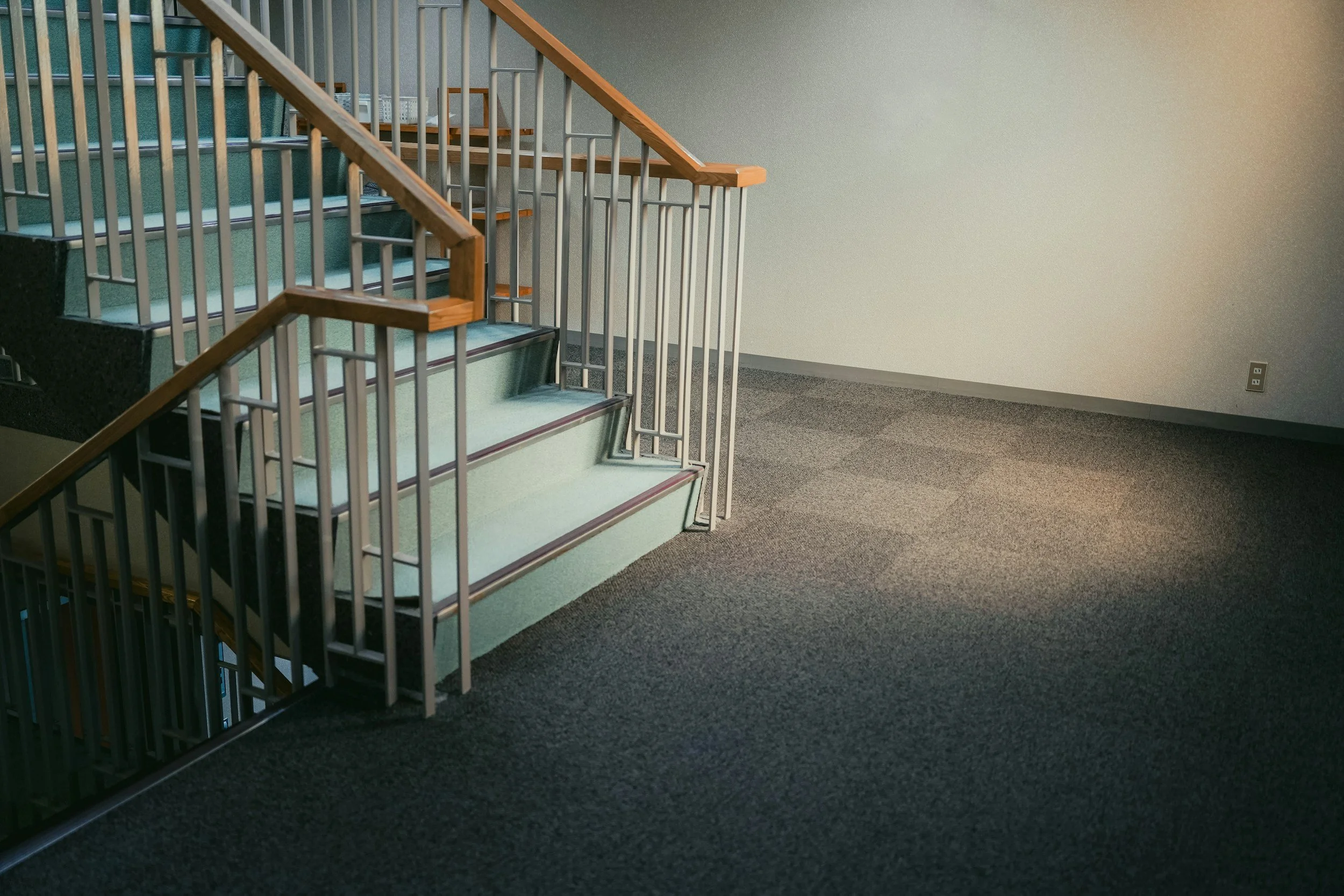 Empty indoor staircase with striped carpet and metal railings located in a spacious, brightly lit corridor.