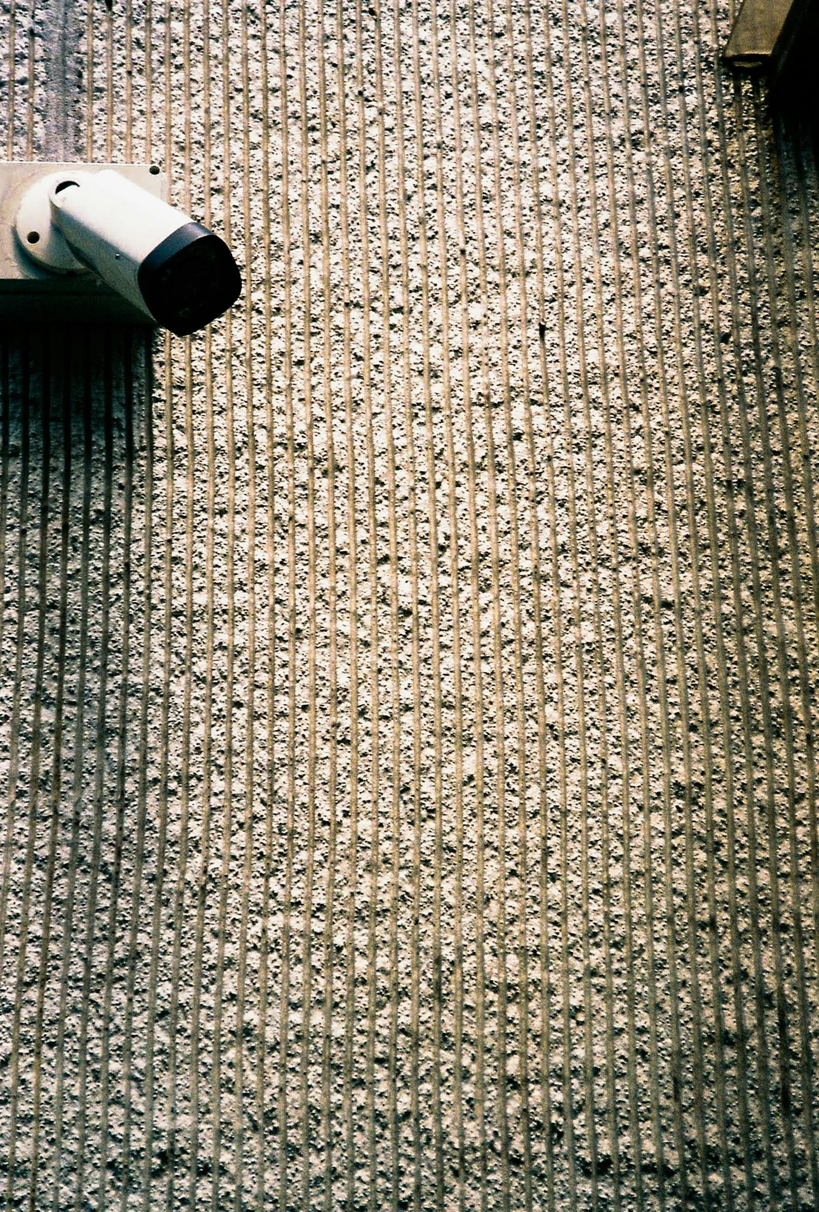 Close-up of surveillance camera mounted on a textured outdoor wall.