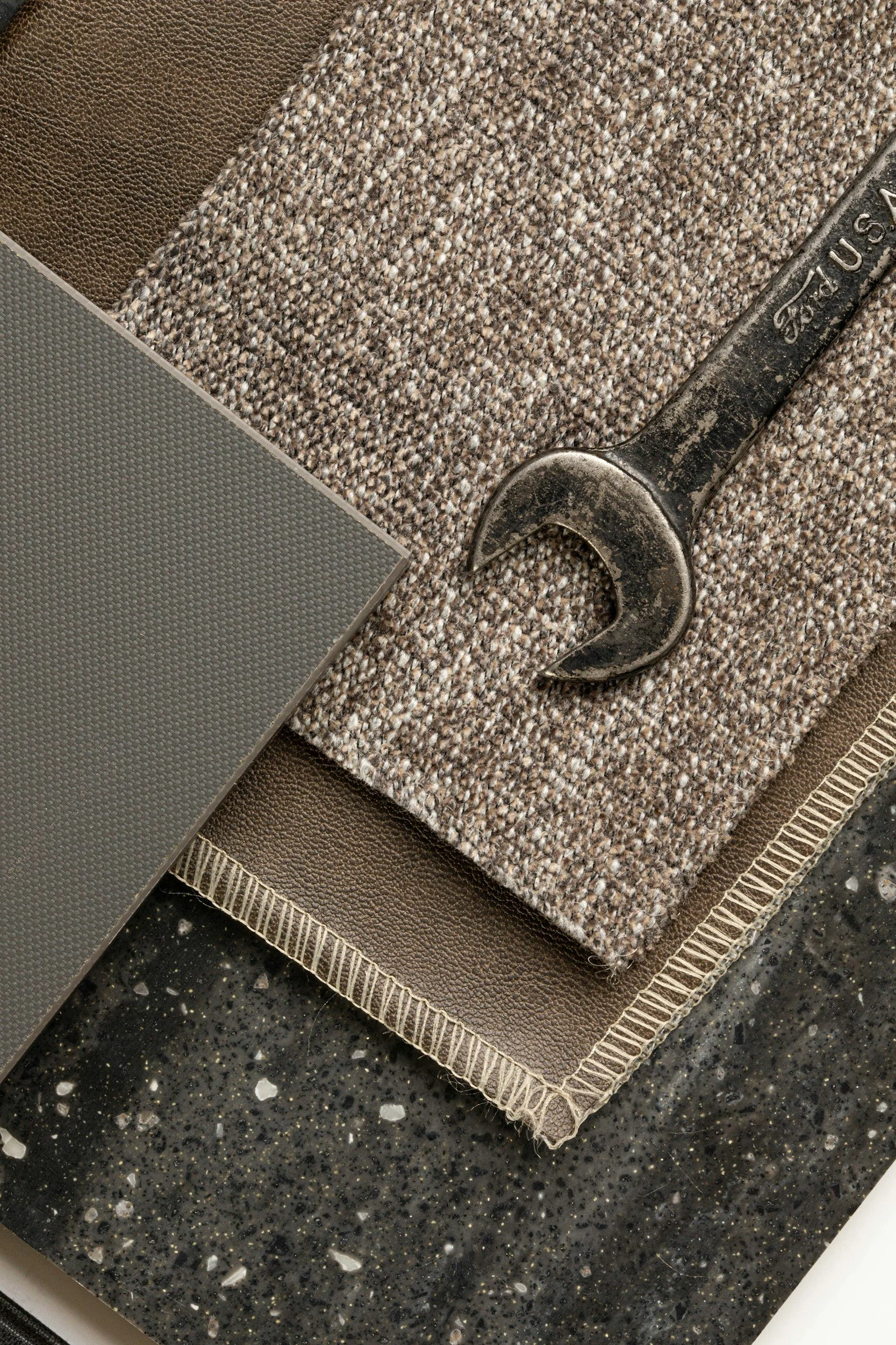 A close-up of fabric samples and a wrench on a black speckled surface.