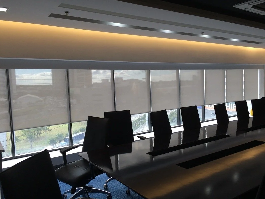 Empty conference room with black chairs around a large meeting table, large windows with blinds, and ceiling lights.