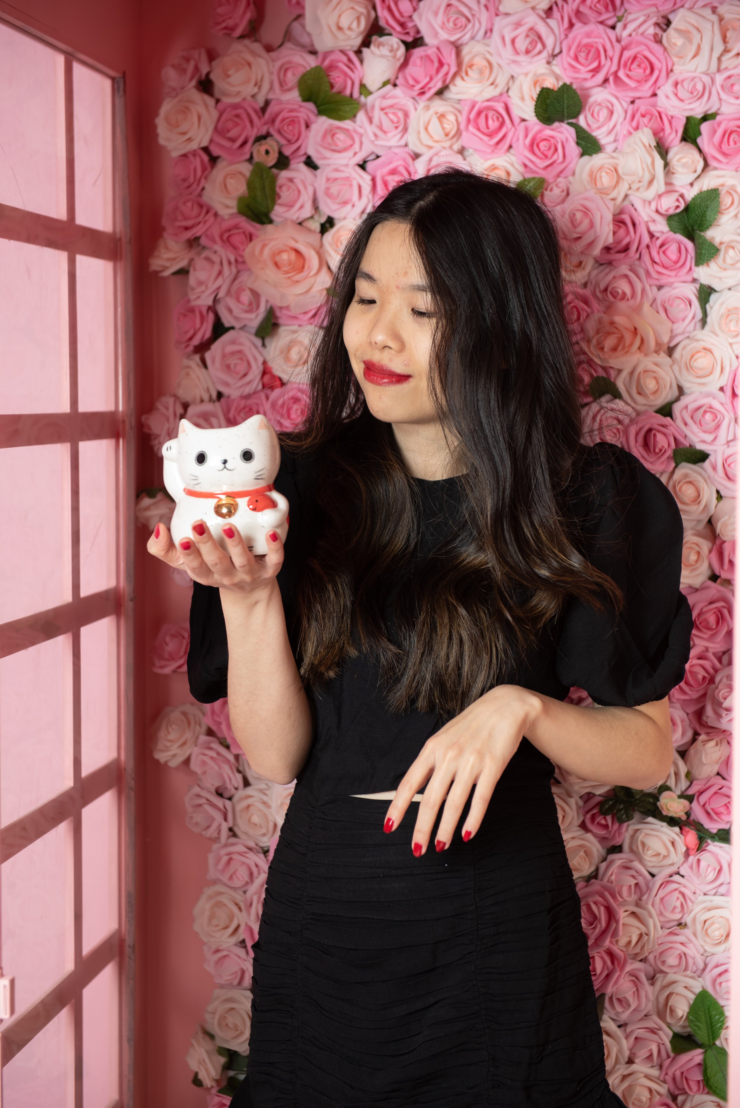 Kimberly Te against a pink floral background, holding and looking down at a cute cat figurine.