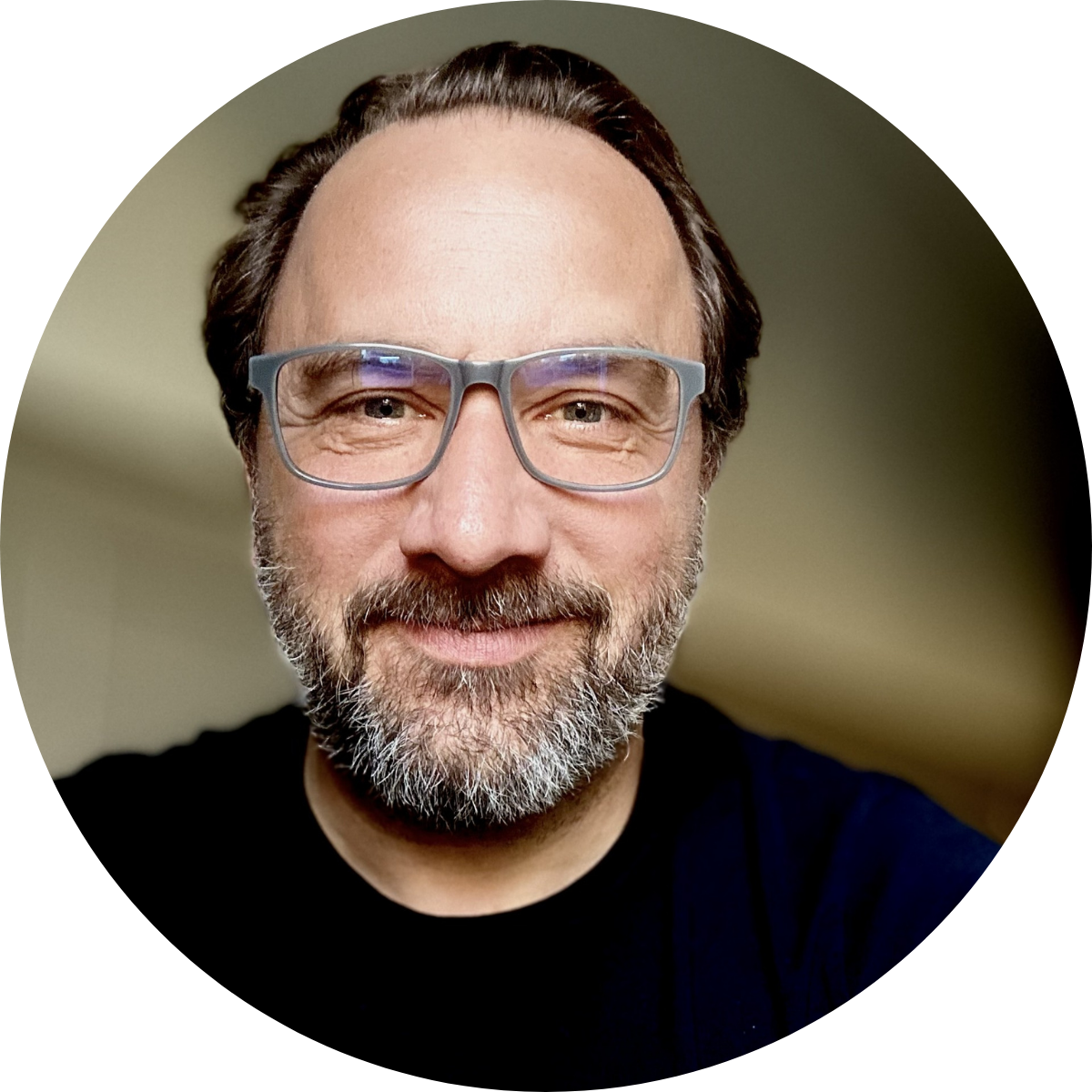 A smiling man with gray hair and beard wearing glasses.