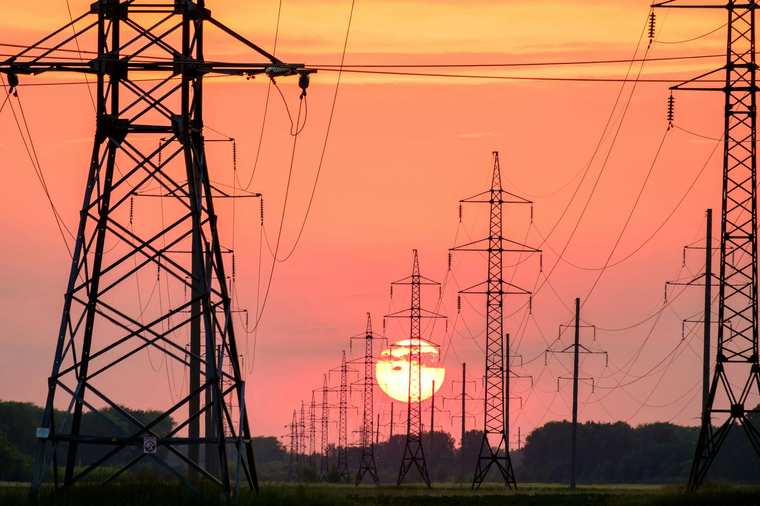 Sunset with orange, pink, and yellow sky behind a series of electrical transmission towers and power lines.