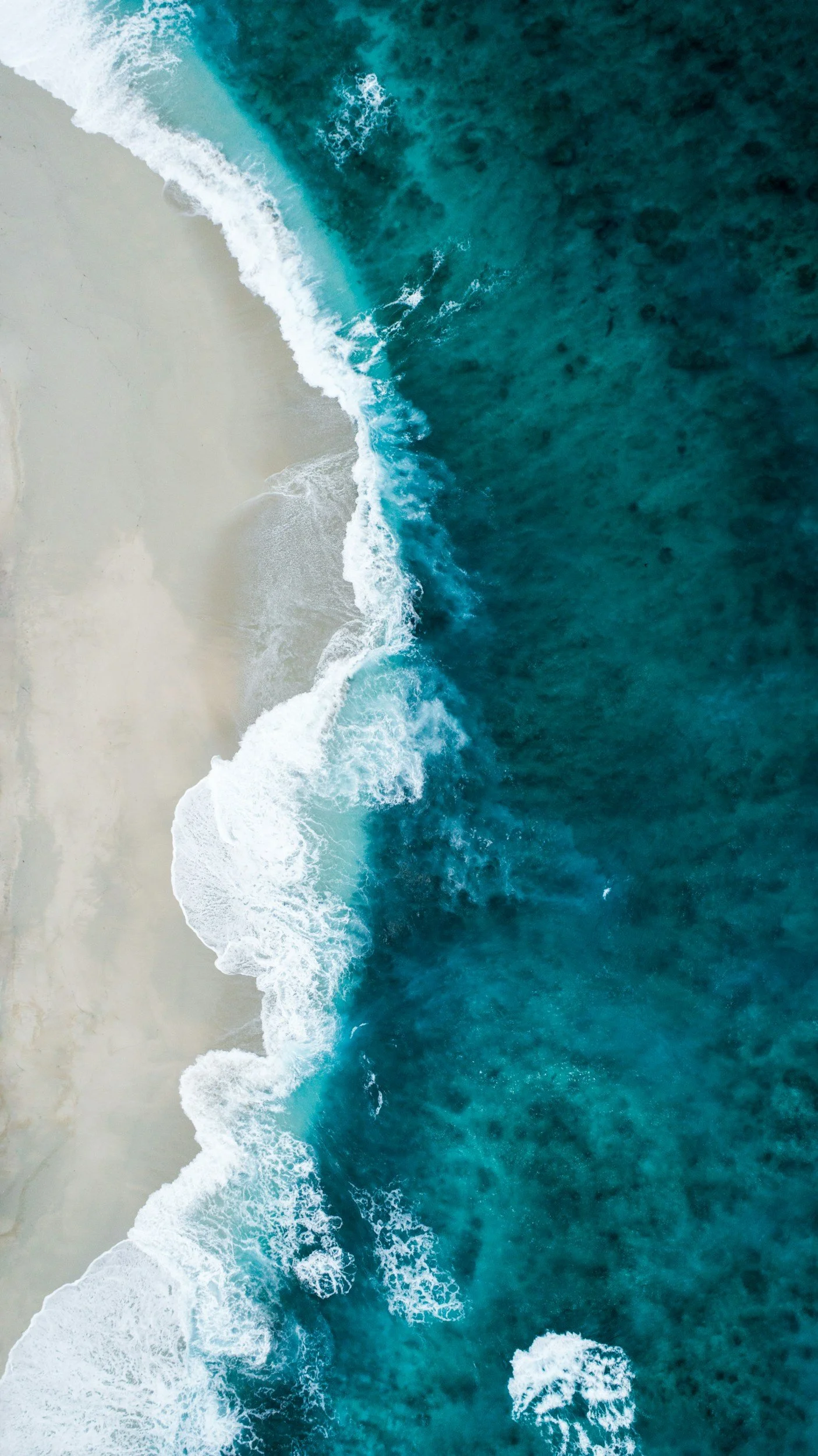 Aerial view of a beach with white sand and turquoise ocean waves crashing onto the shore.