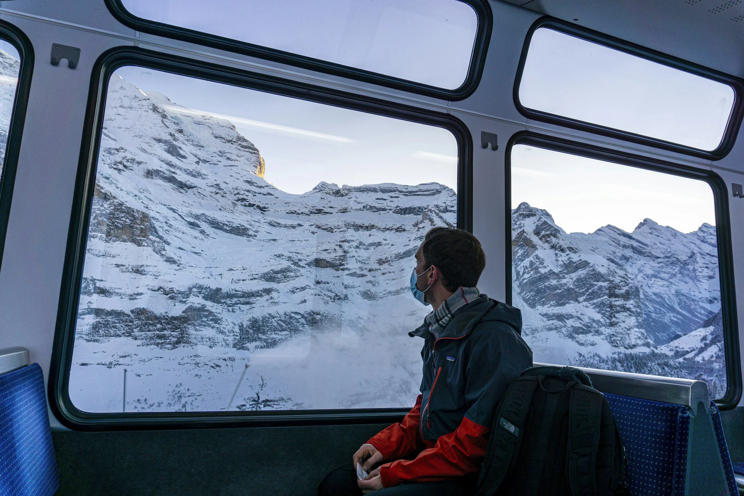 Person sitting on a bus looking out the window at snow-covered mountains.