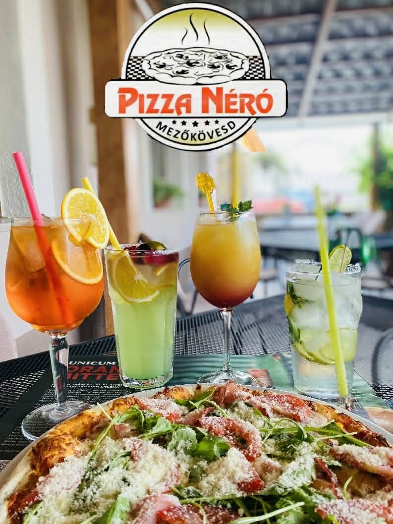 A table with a pizza topped with arugula, shredded cheese, and tomatoes, along with four colorful cocktails garnished with lemon, cherry, mint, and decorative stirrers, at Pizza Néro restaurant.