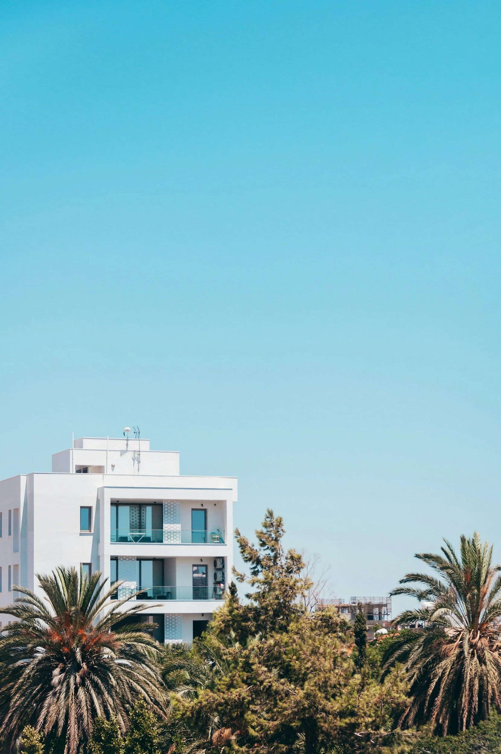 White modern apartment building, surrounded by palm trees, under a clear blue sky.
