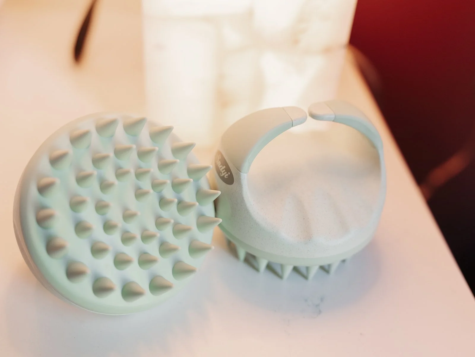 A light green massage roller with rounded spikes on one side and a curved, open handle, resting on a white surface.