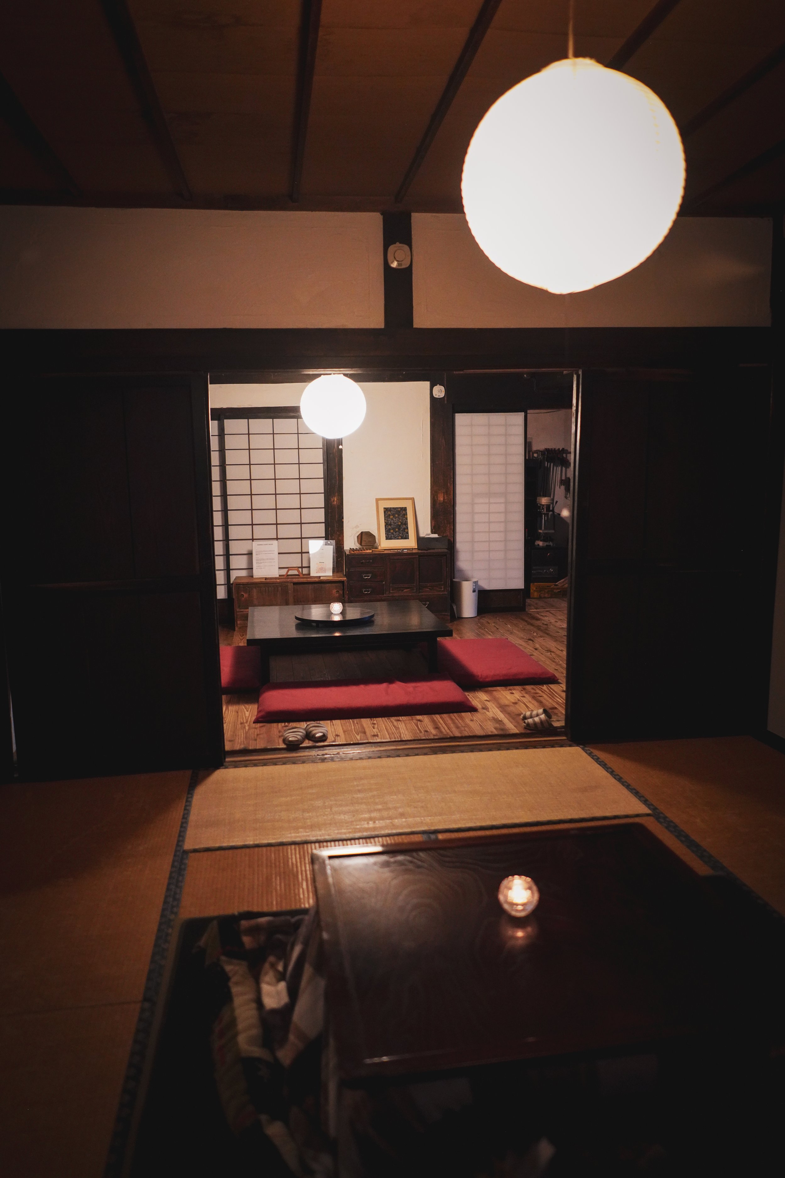 A traditional Japanese interior with tatami mats, a low wooden table, cushions, and shoji sliding doors. Soft lighting creates a cozy atmosphere.
