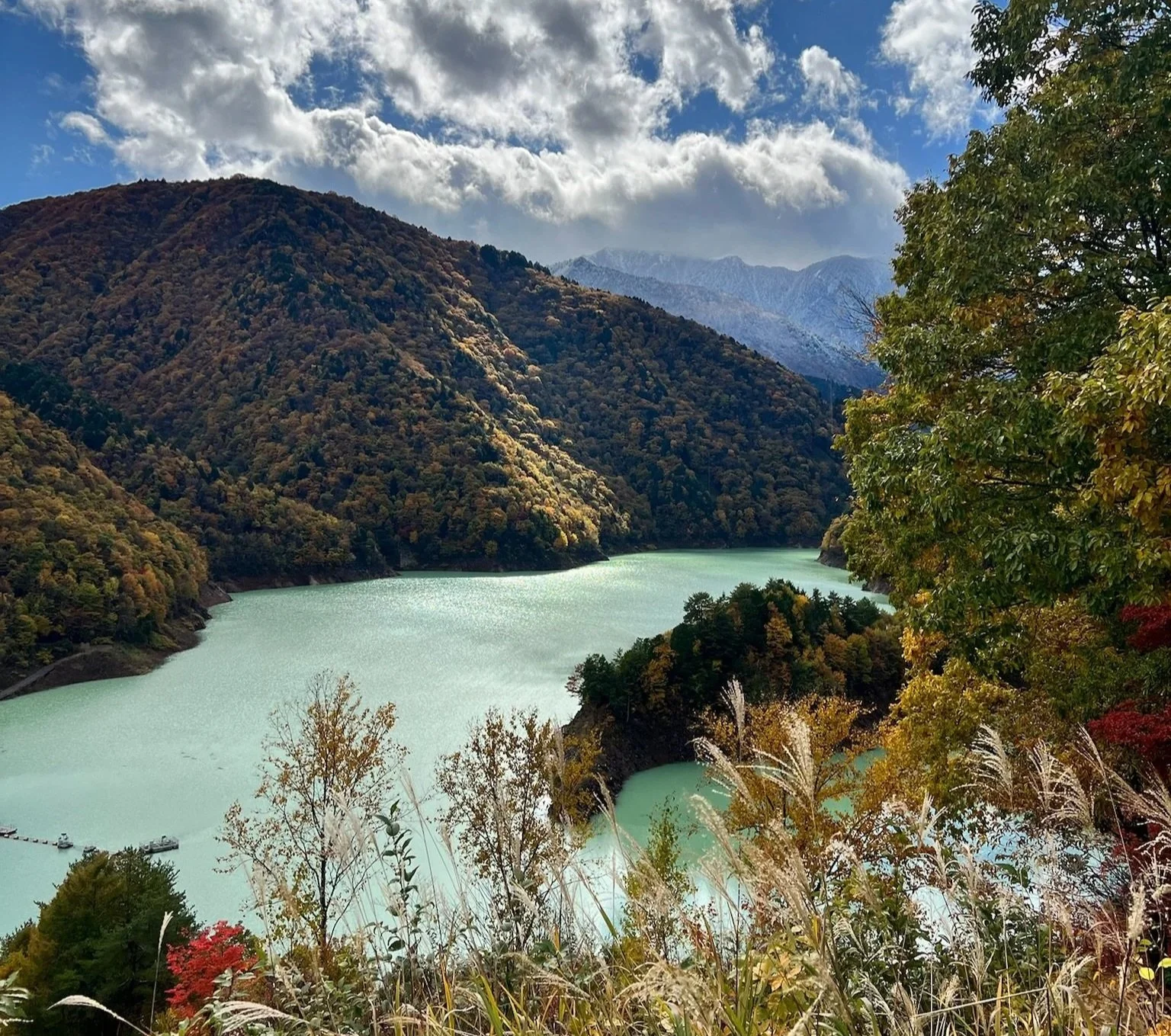 Scenic view of a winding river in a mountainous area with autumn foliage, partly cloudy sky, and a snowy mountain in the distance.