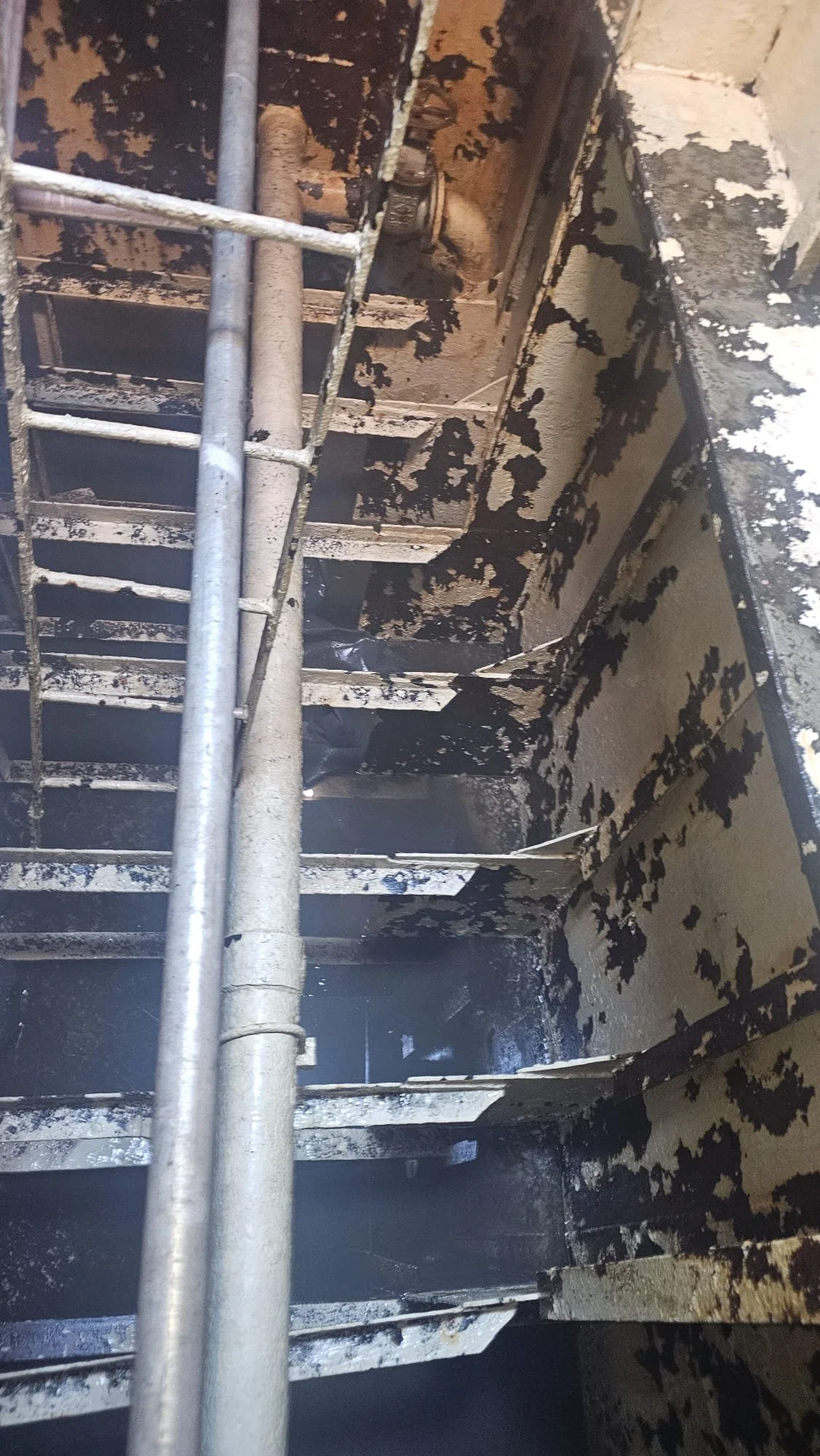 Charred staircase with burnt and peeling paint, and a metal handrail, suggesting recent fire damage.