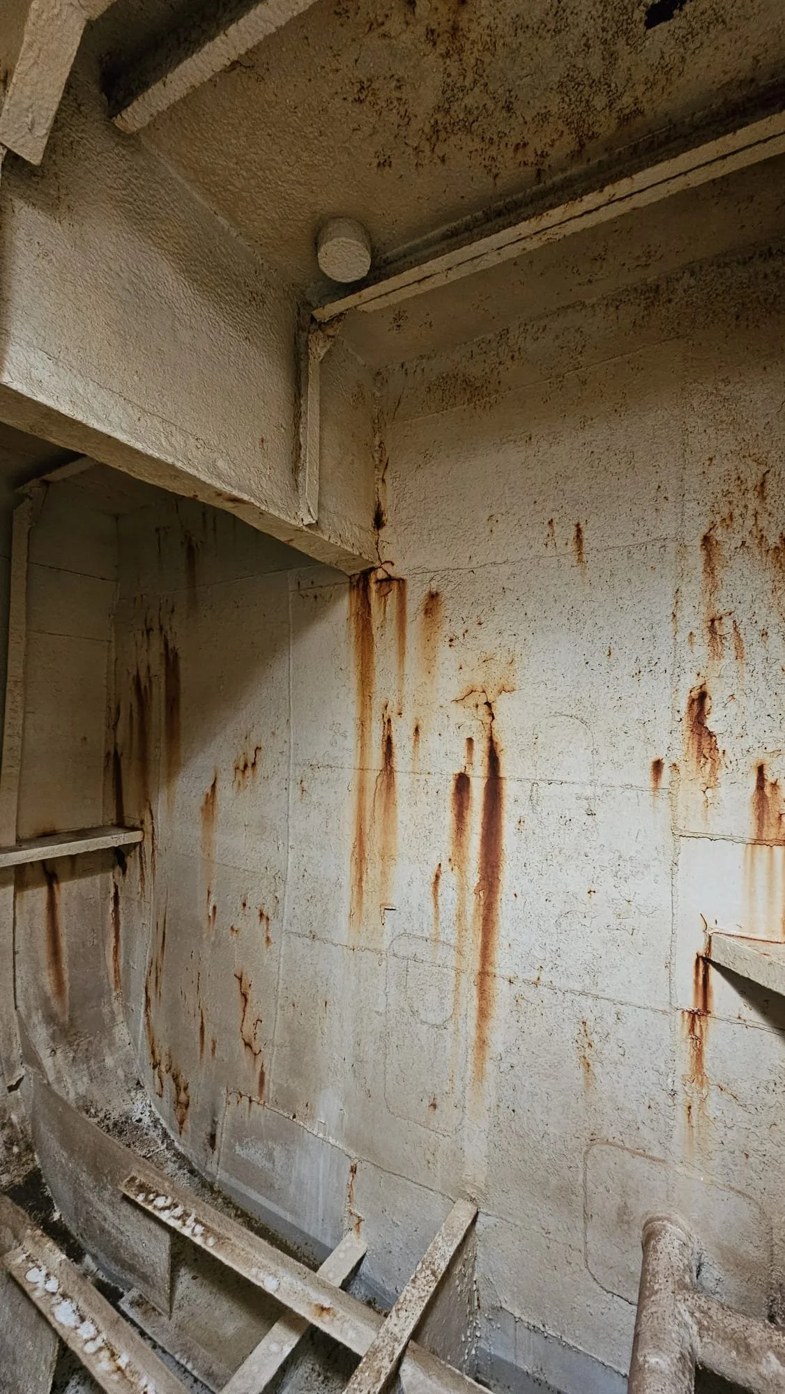 A wall with rust streaks downward from the ceiling, showing signs of water leakage and corrosion in an industrial or basement setting.