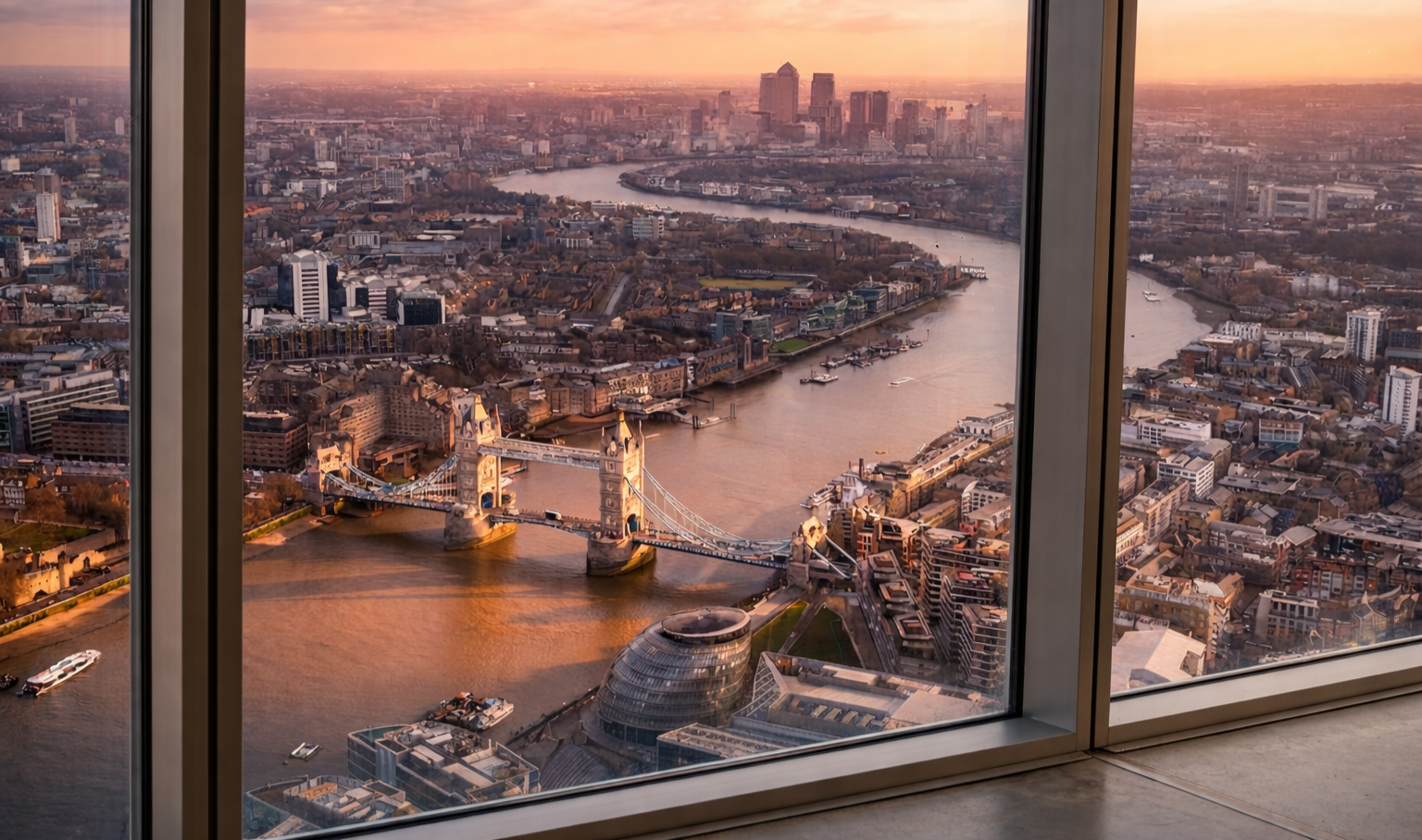 Aerial view of London at sunset showing the River Thames, Tower Bridge, City Hall, and the surrounding cityscape.