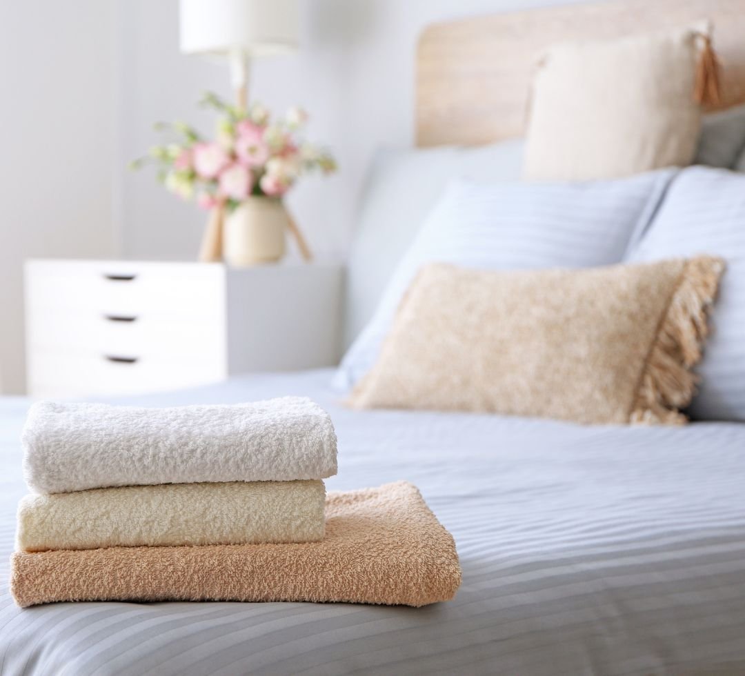 Toallas suaves dobladas sobre una cama con ropa de cama clara en un dormitorio moderno.