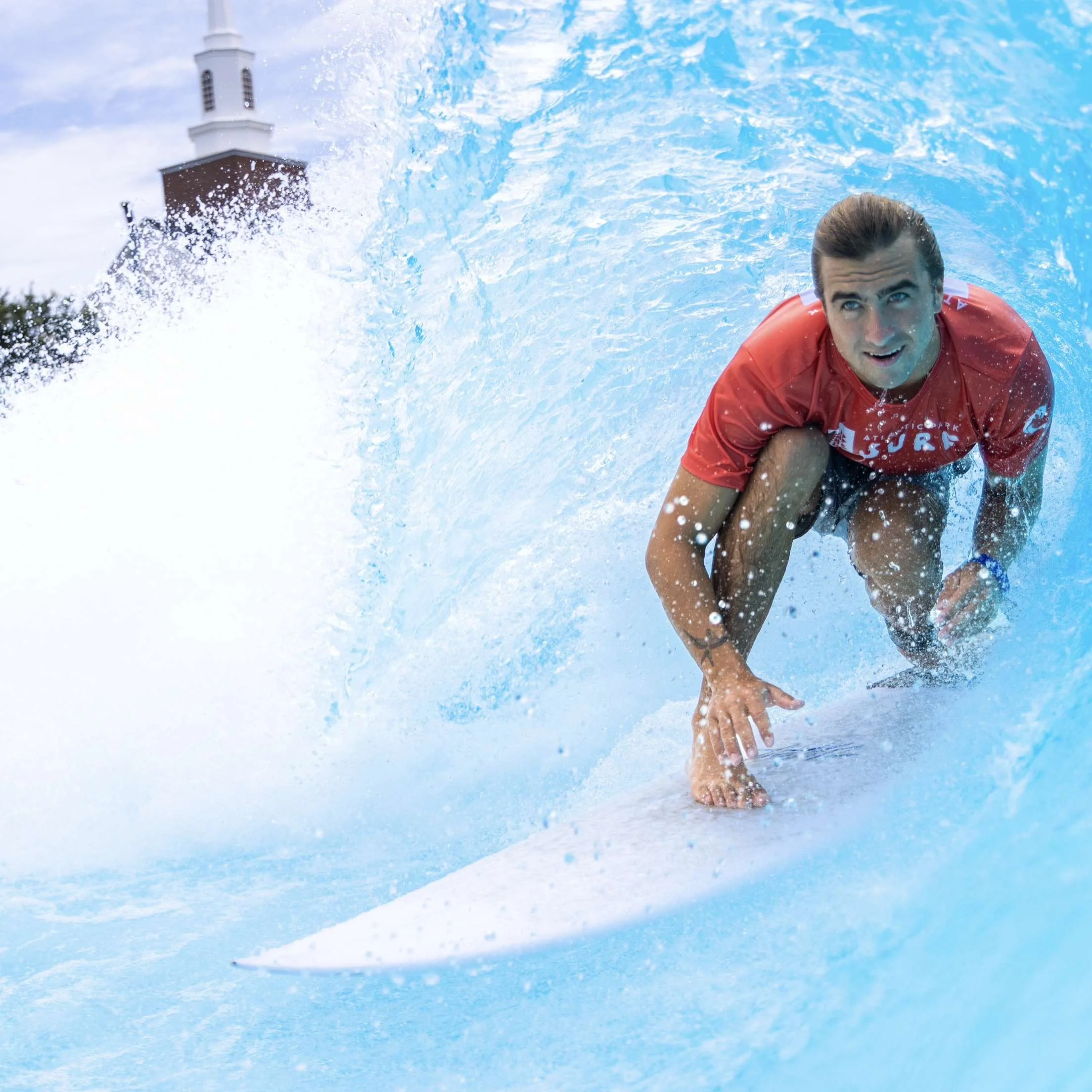 Man surfing on a wave with a church steeple in the background.