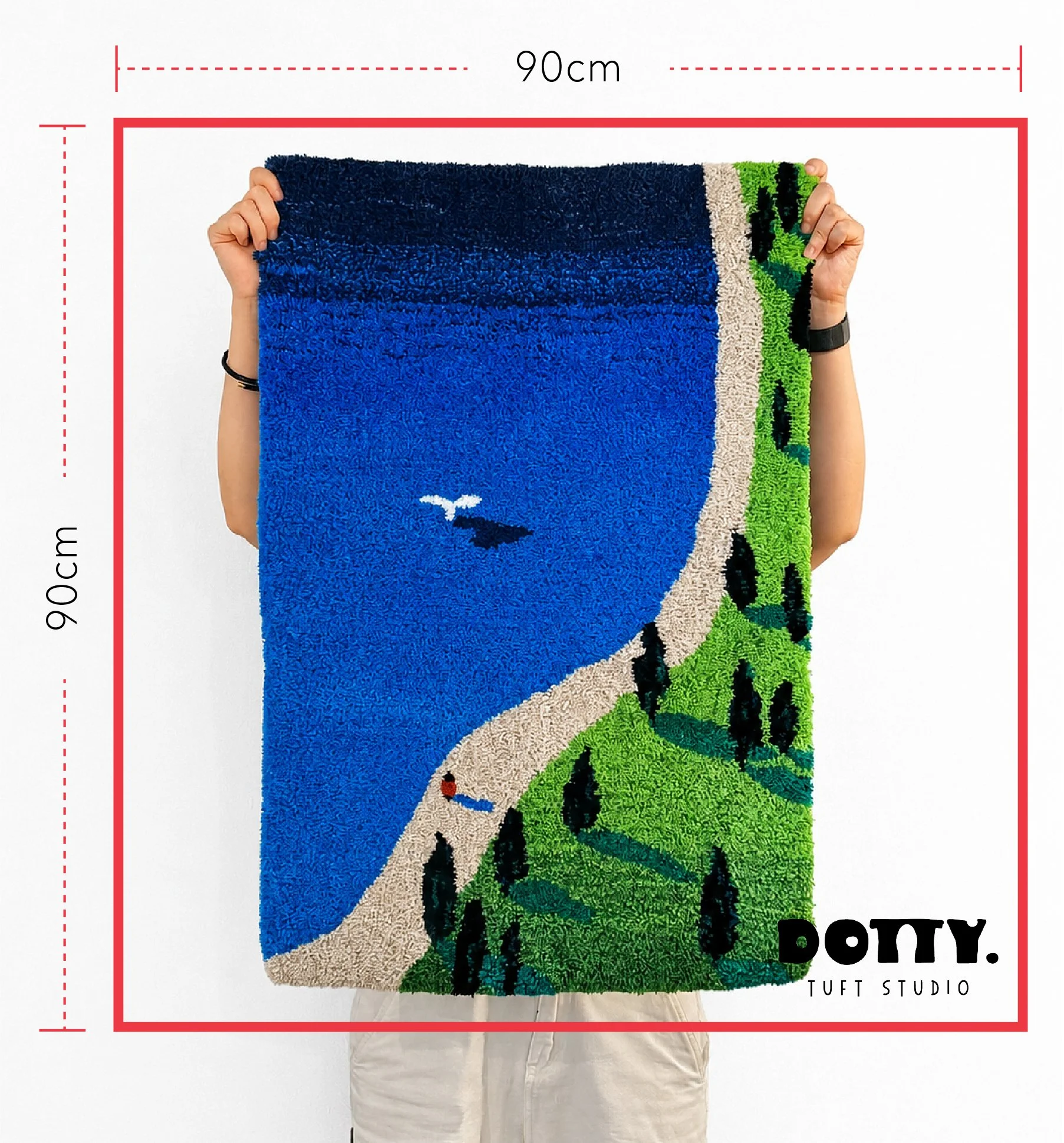 A person holding a colorful quilt with a beach scene design, featuring a whale and seagull, showing available tufting frame sizes for workshop measuring 90 cm by 90 cm at Dotty Tuft Studio.