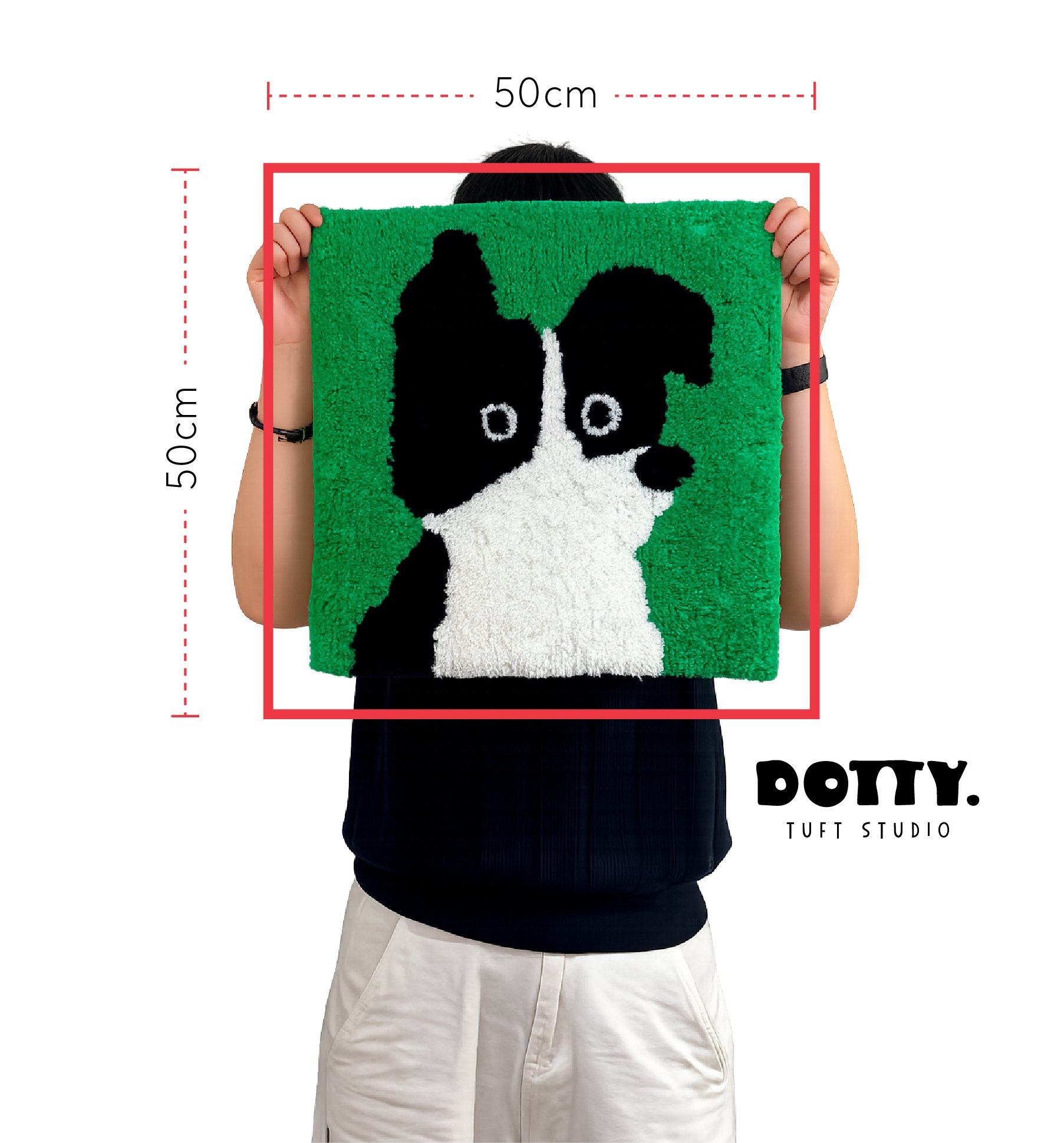 Person holding a green rug with a black and white dog face design, showing available tufting frame size for workshop measuring 50 cm by 50 cm at Dotty Tuft Studio.