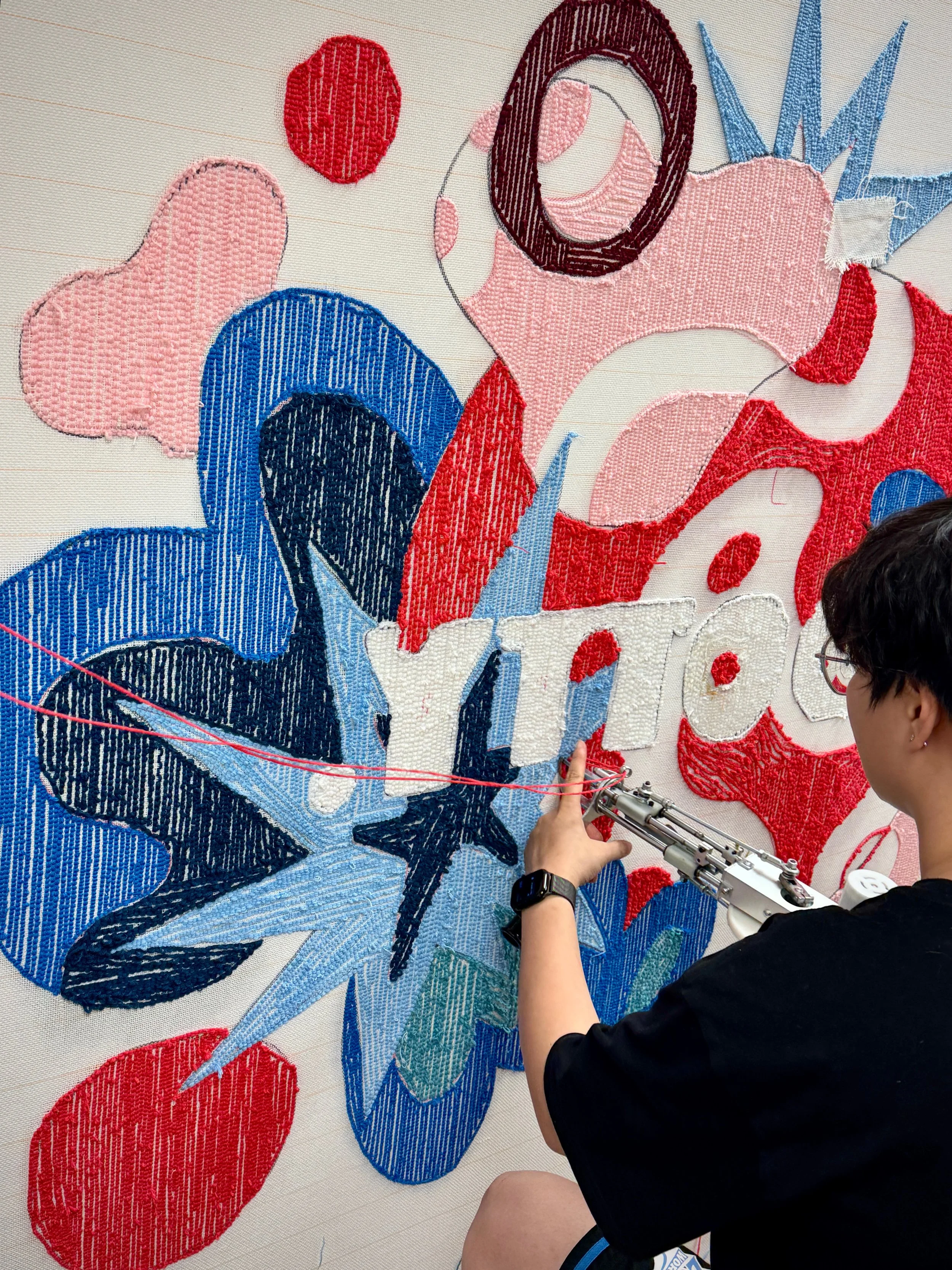 A person working on a large, colorful tufting artwork hanging featuring Dotty Tuft Studio.