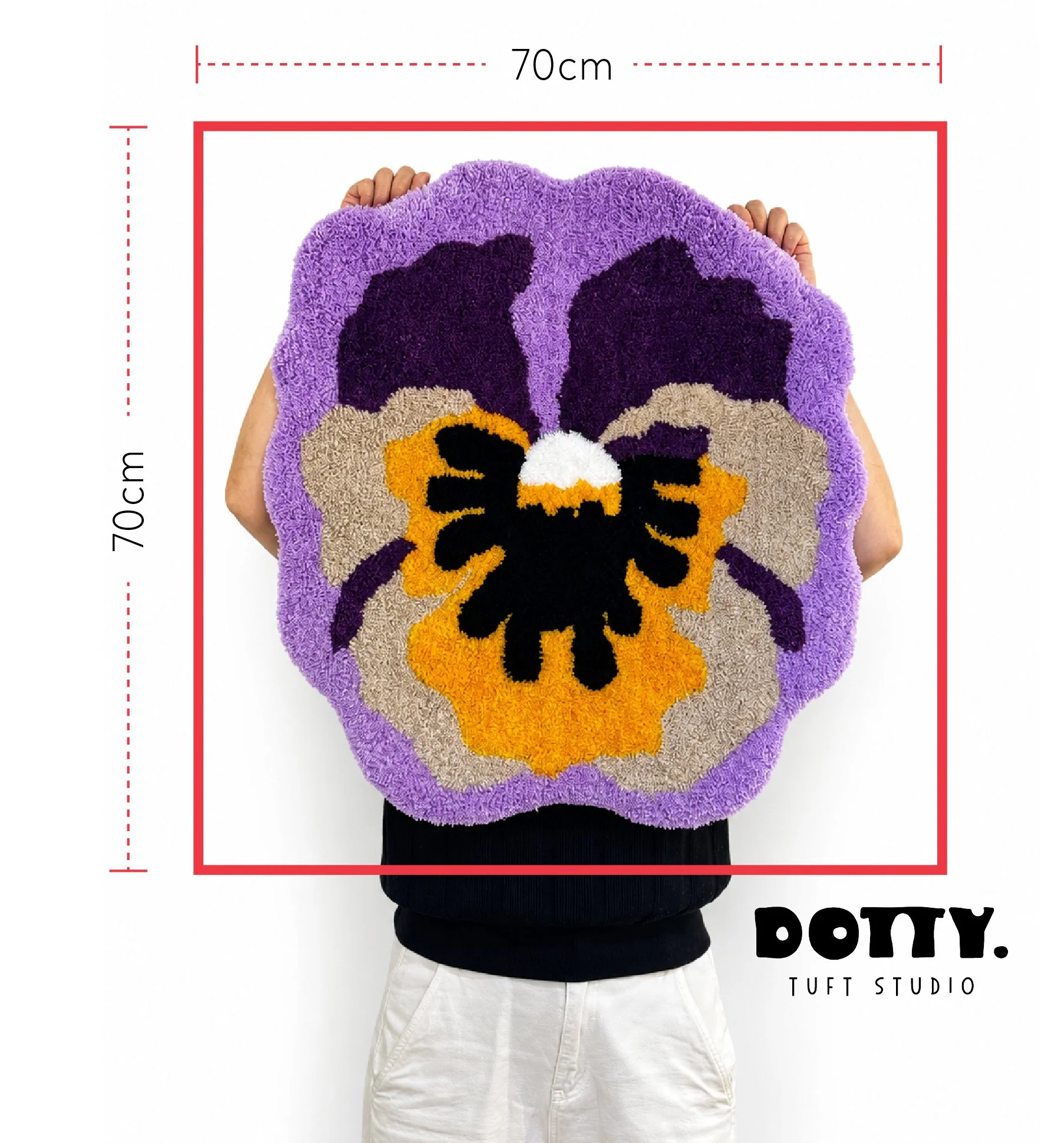 Close-up of a person holding a colorful, patterned rug with a purple border and black, beige, and orange filling, showing available tufting frame sizes for workshop measuring 70 cm by 70 cm at Dotty Tuft Studio.
