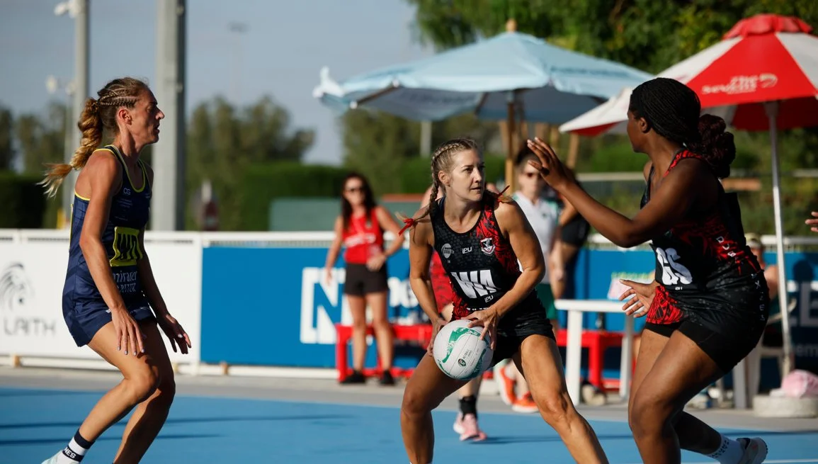 Three female netball players in action during a match at the dubai rugby sevens at the 7s stadium in Dubai with a Gilbert netball ball and apparel.