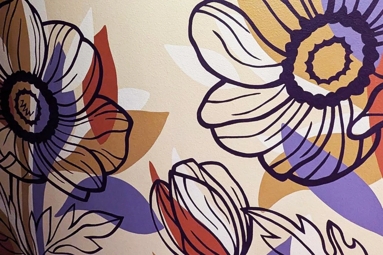 Wallwork Studio mural in progress, featuring large outlined flowers in purple, beige, and red on a light wall.