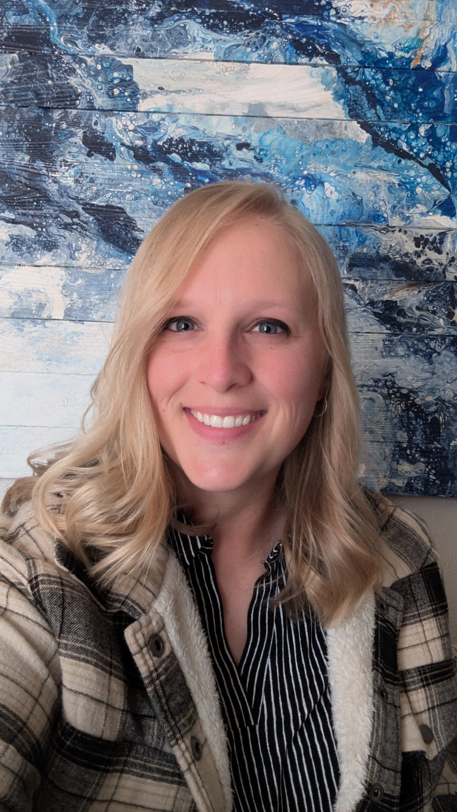 Kylee Smit, founder of Strata Nova Studio, smiling in front of a blue abstract painting.