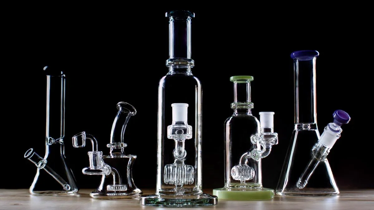 Collection of various glass bongs and water pipes on a wooden surface with a dark background.