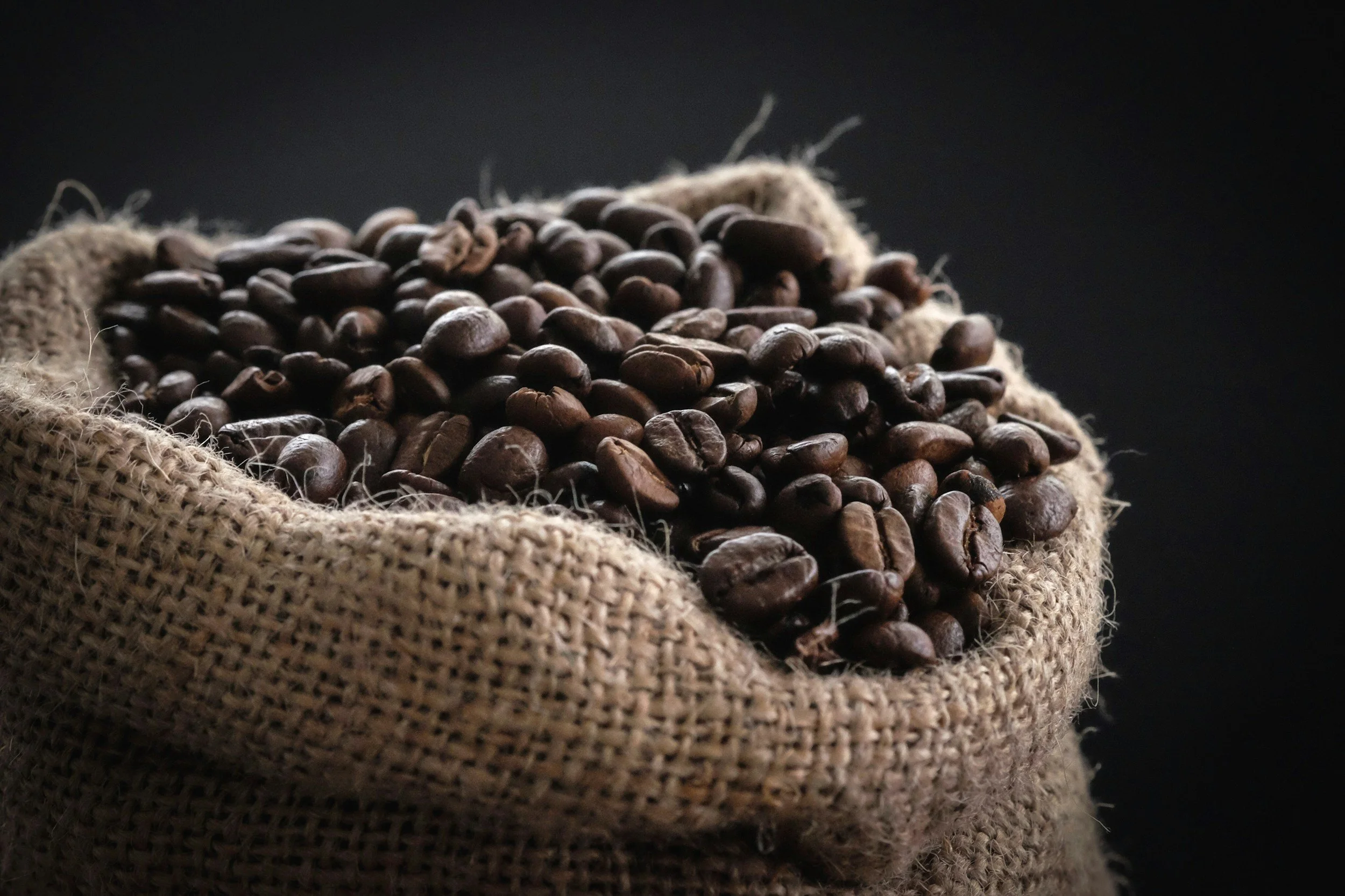 Close-up of roasted coffee beans in a burlap sack against a black background.