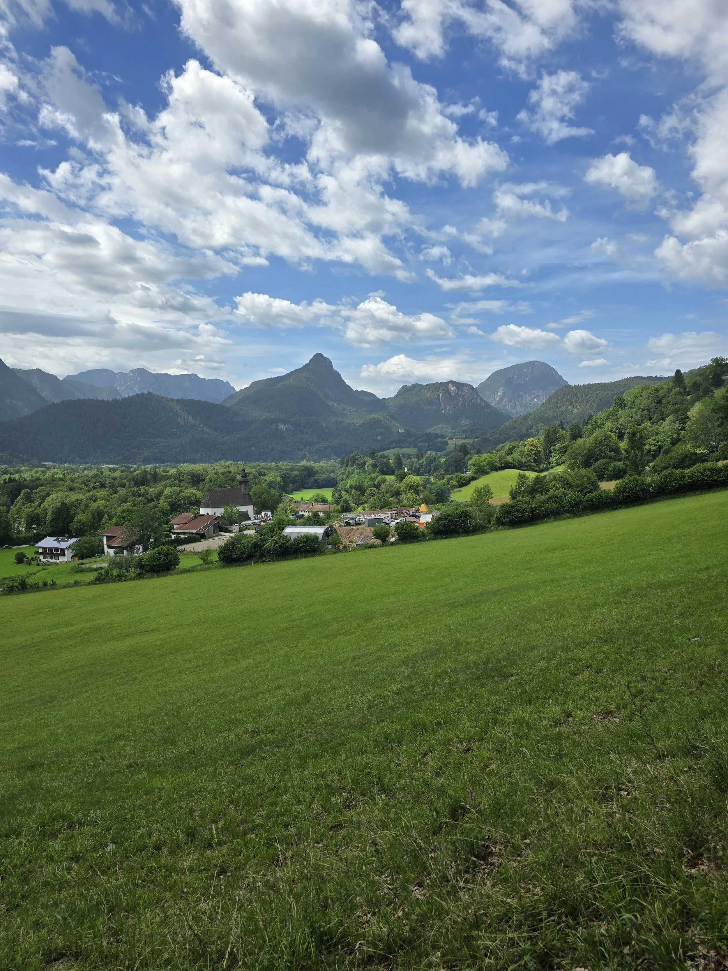 Blick über eine grüne Wiese auf Berge im Berchtesgadener Land unter wolkigem Himmel.