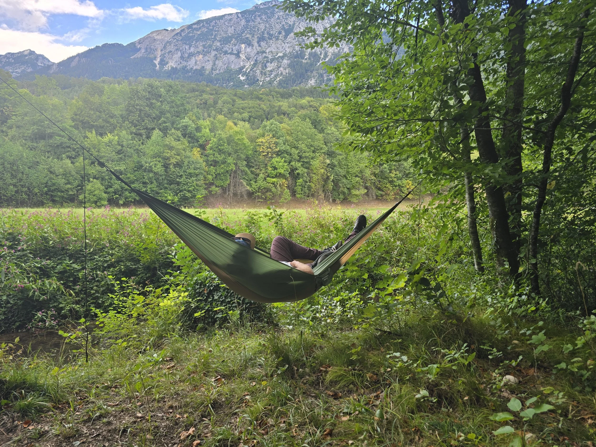 C. entspannt in einer Hängematte im Grünen und genießt die Ruhe in der Natur.
