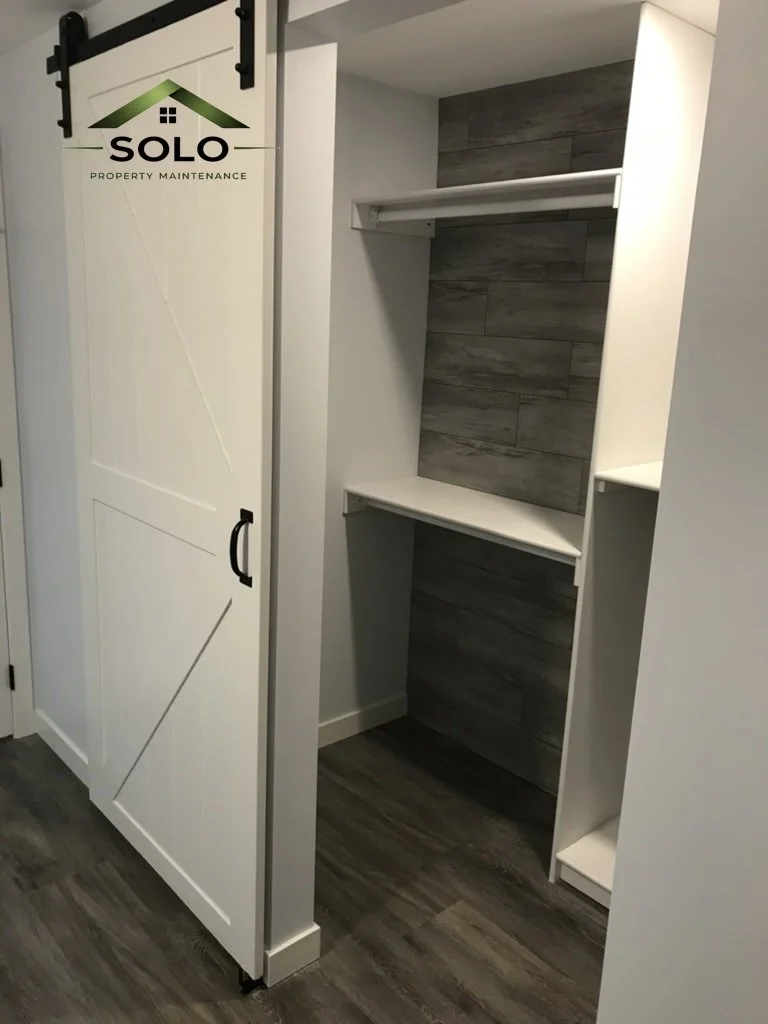 Empty built-in closet with white shelves and a hanging rod, next to a sliding barn door with black hardware in a modern home interior.