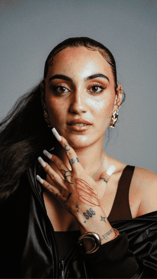 Portrait d'une femme avec maquillage, bijoux, tatouages, portant une veste en cuir, en fond gris