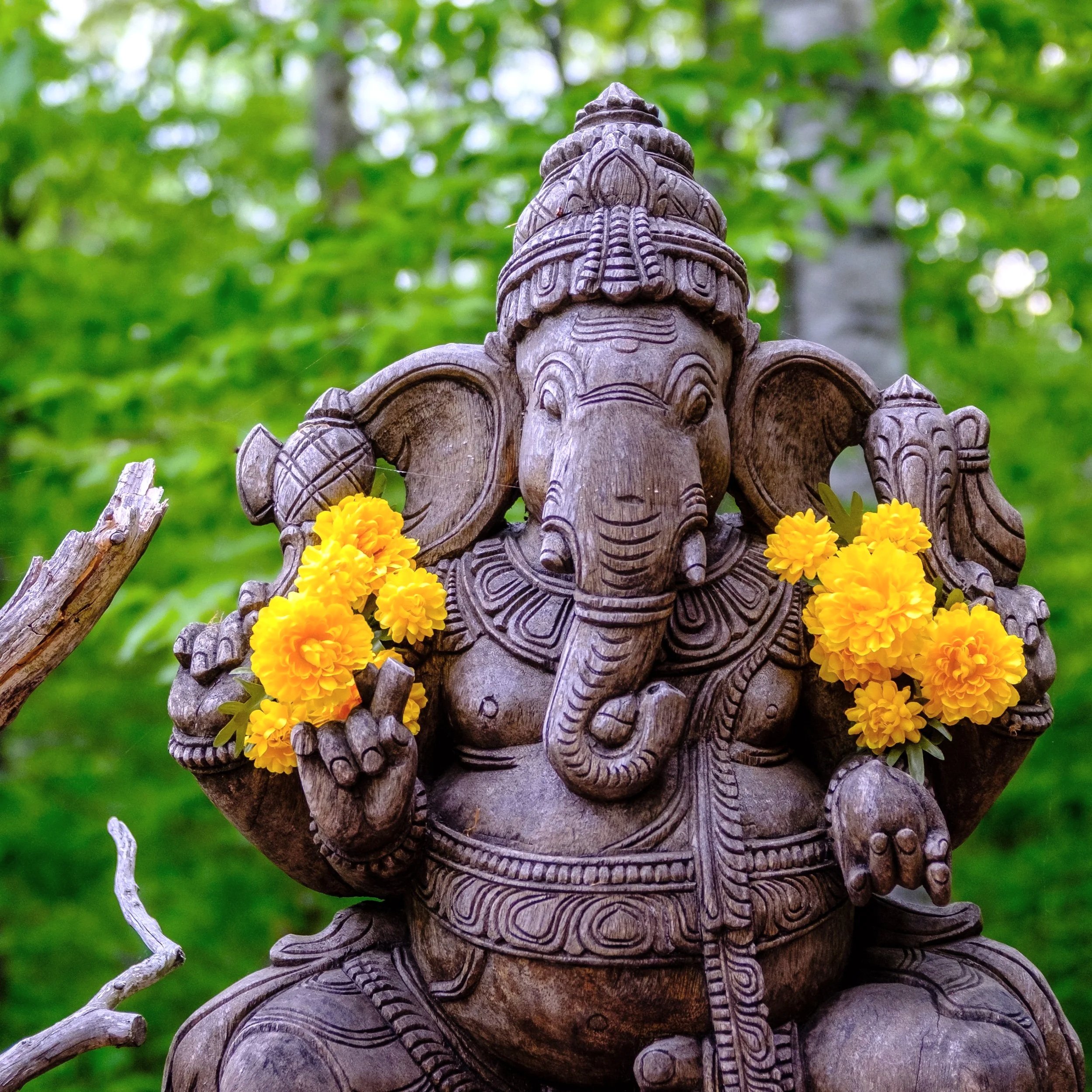 A wooden Ganesh Deity with yellow flowers