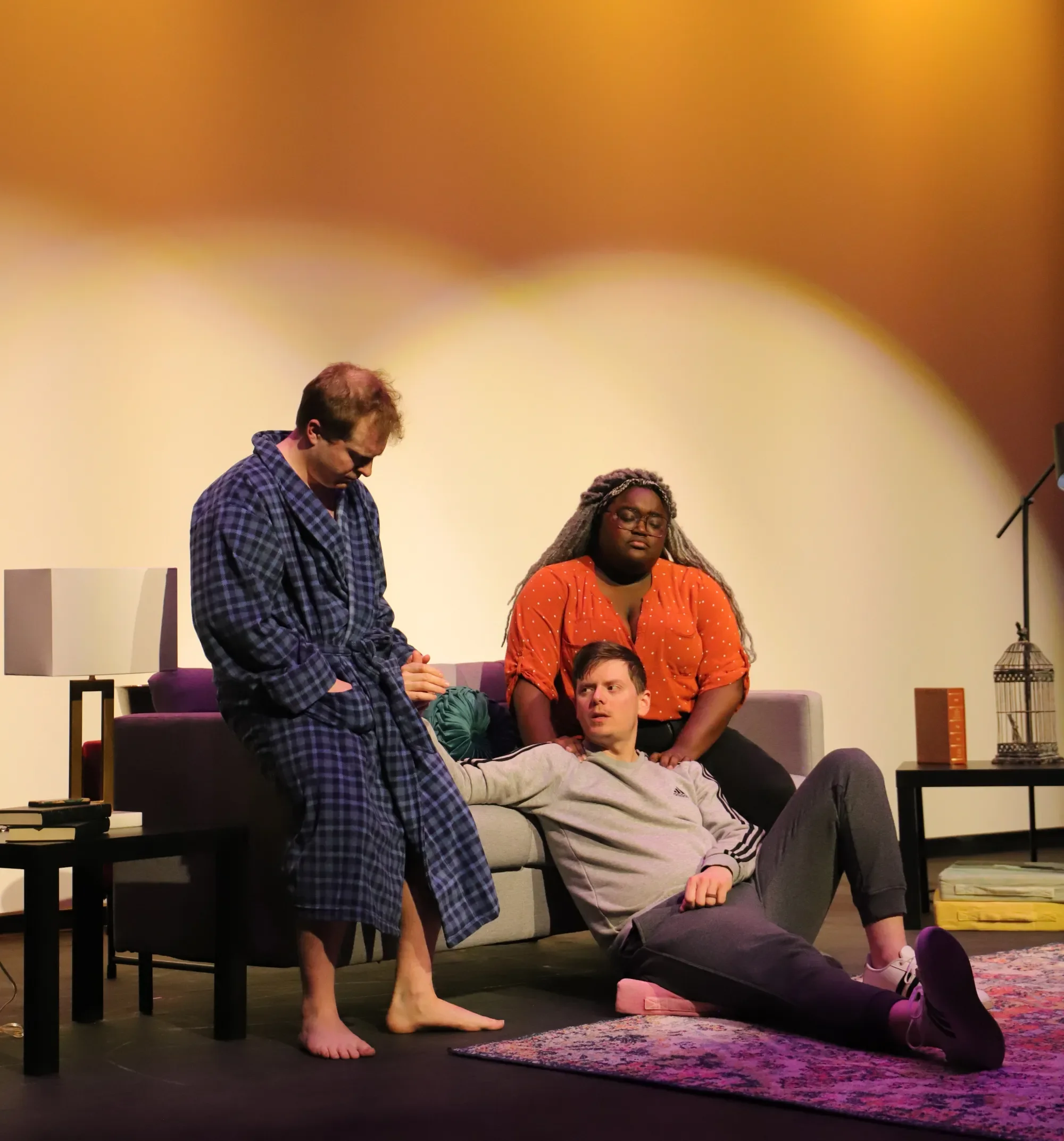 Three actors in a living room set from KC Public Theatre's production of The Holy Trinity, a new play with dramaturgy by soph marsh.