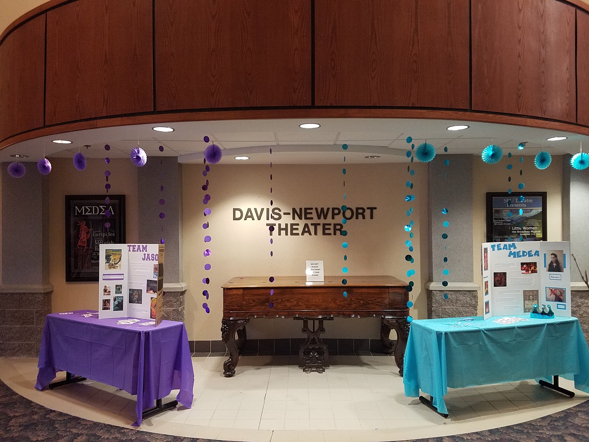 Interior of the Davis-Newport Theater with decorations and display tables for an event, featuring purple and teal tablecloths and hanging paper decorations.