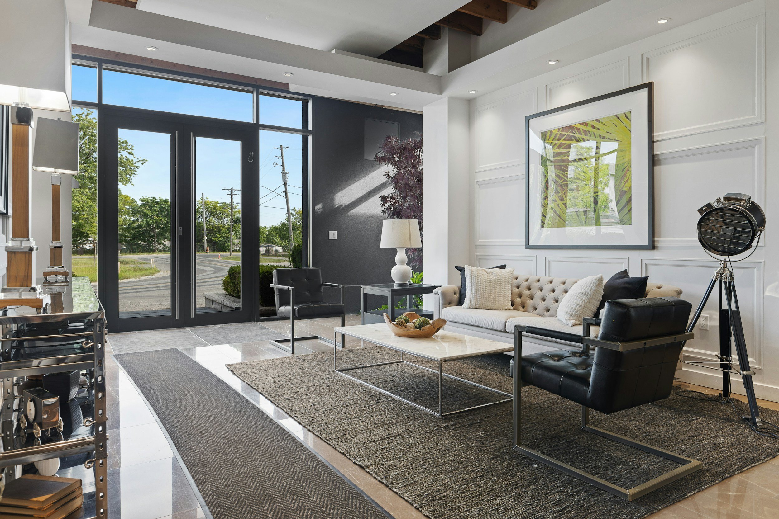 Modern hotel lobby with glass front doors, white and black furniture, a large framed artwork, a floor lamp, and a large floor light.