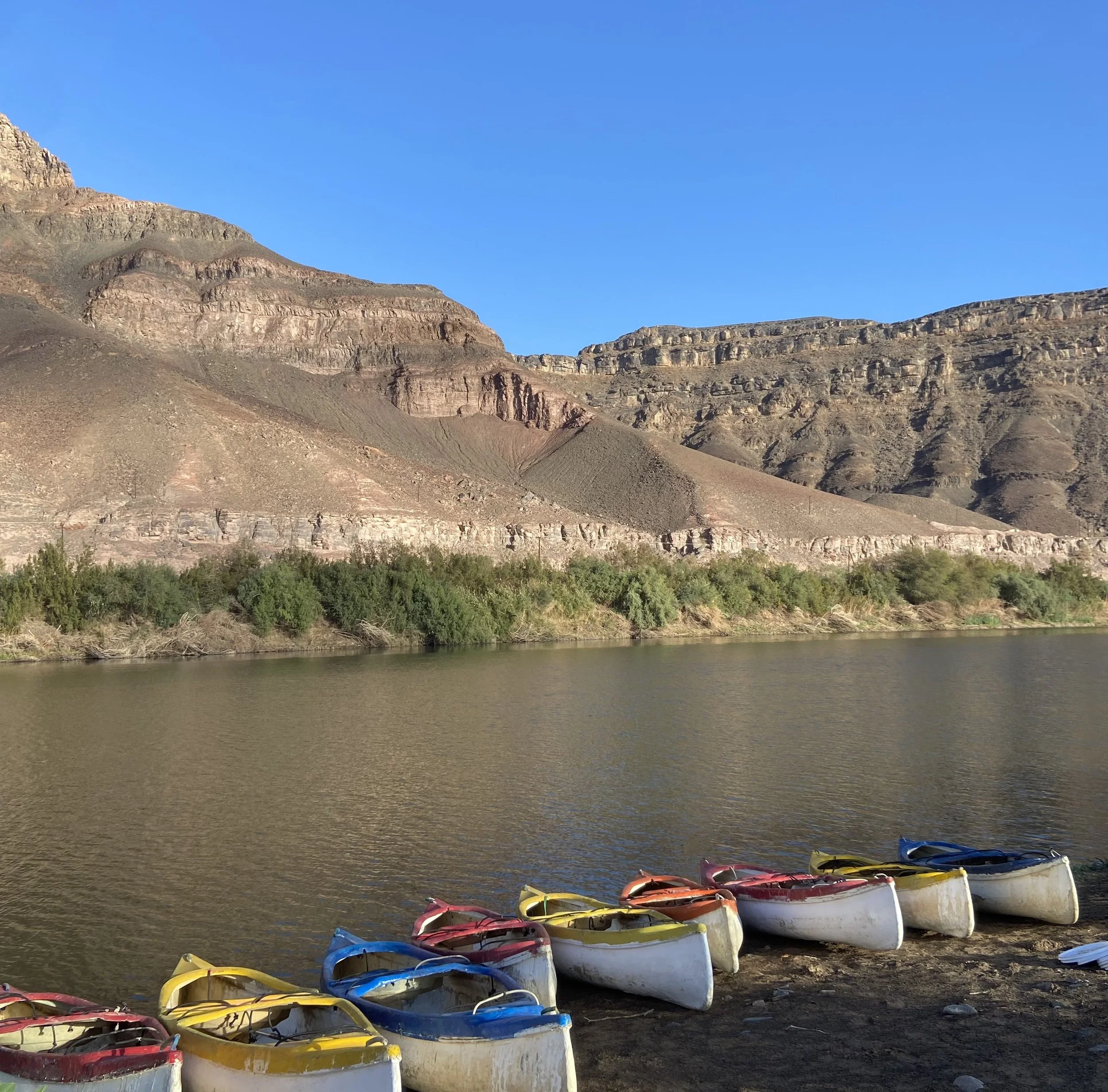 Colourful kayaks lined up on the bank of the Orange River near Richtersveld surrounded by dramatic desert canyon cliffs.