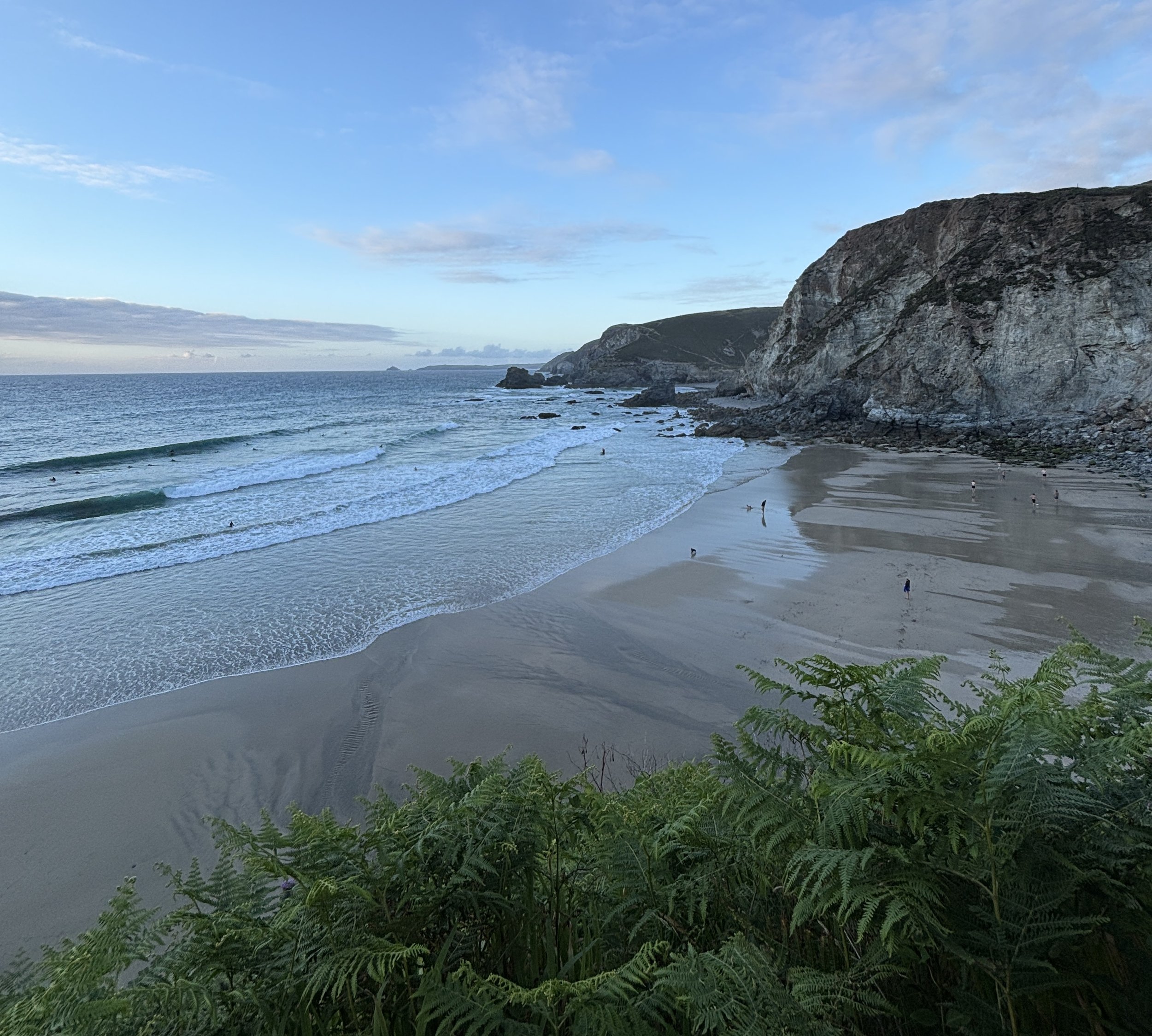 St Agnes from the cliffs above, waves break as surfers wait for waves and people play on the beach