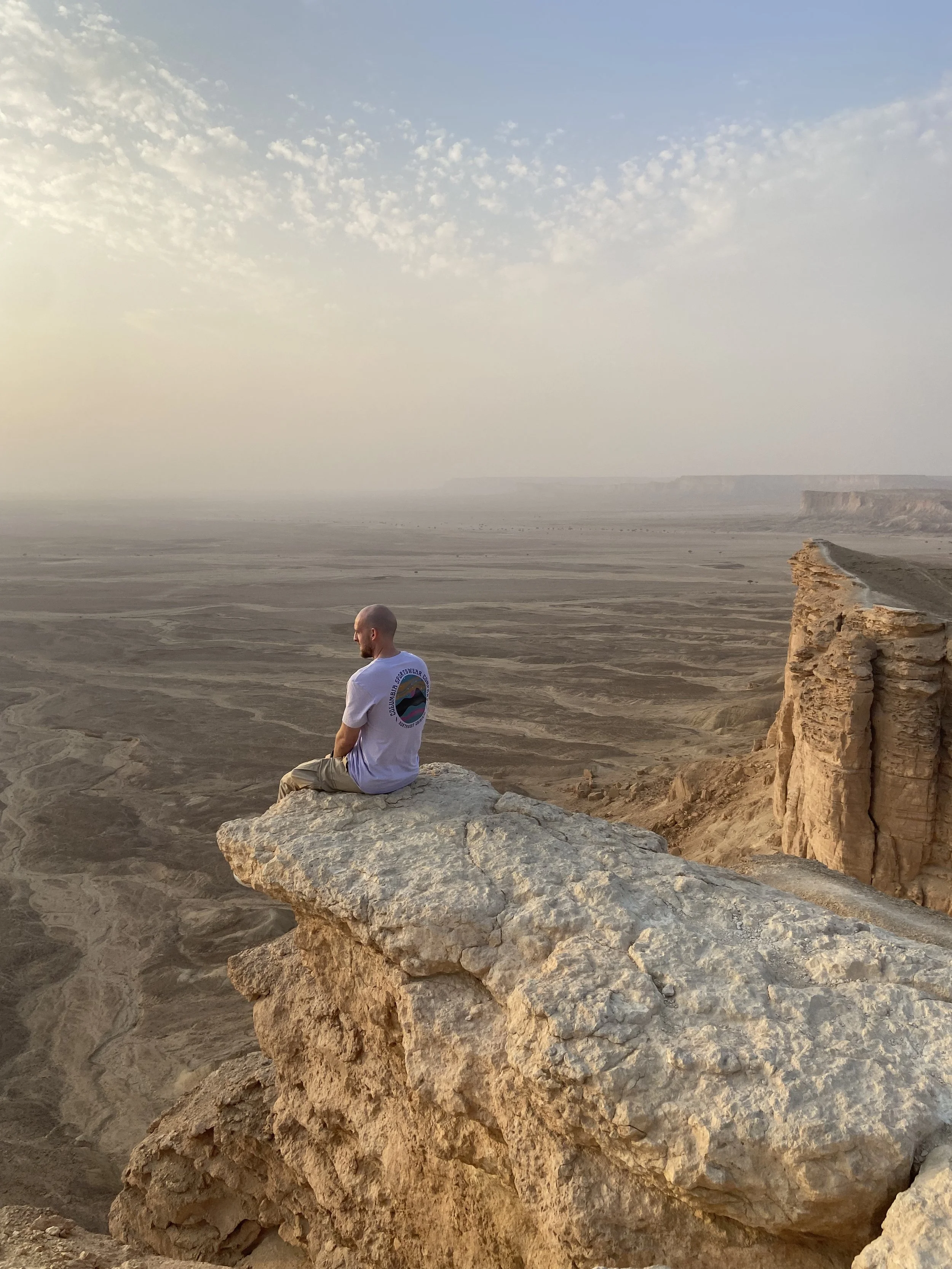 Holocene founder sitting on a cliff overlooking "The edge of the world" that used to be a vast sea in Saudi Arabia  with scattered clouds.