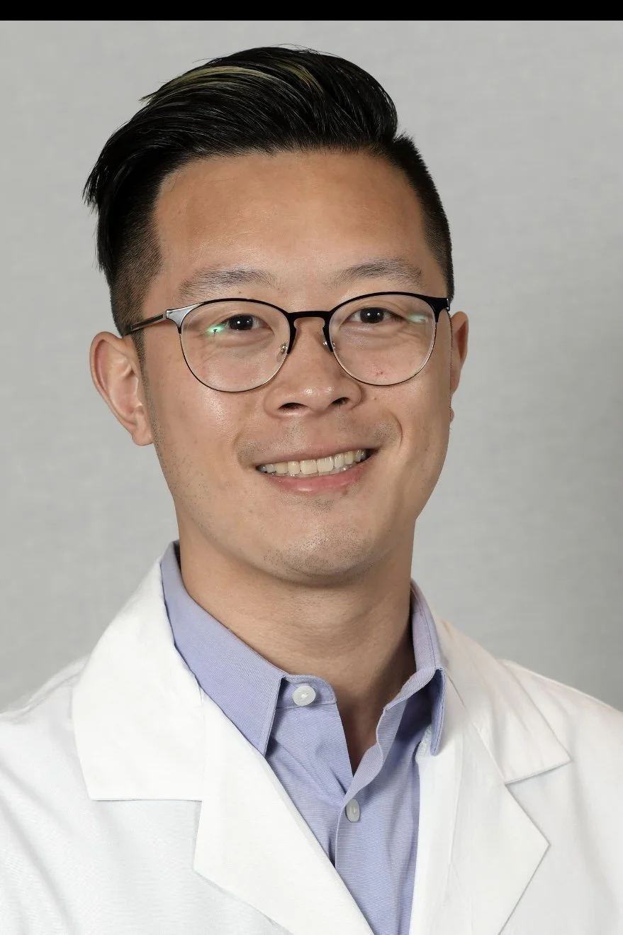 Portrait of a man wearing glasses and a white lab coat, smiling, against a plain background.