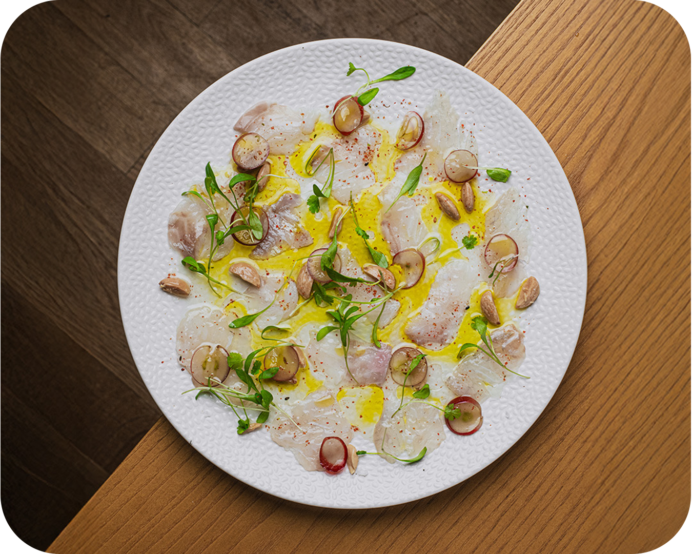 Ensalada de carpaccio de pescado con semillas, microverdes y aceite de oliva sobre plato blanco.