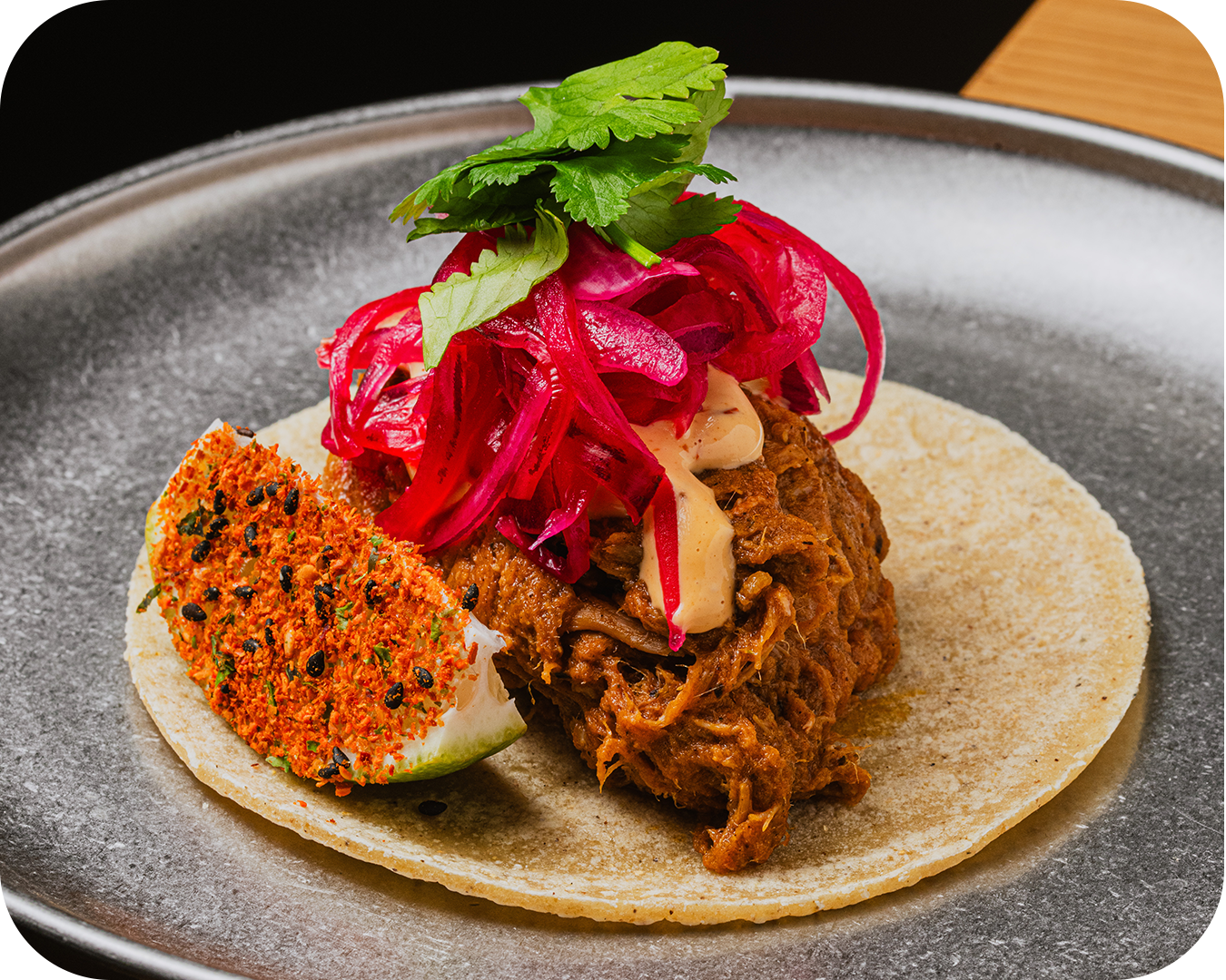 Taco con carne deshebrada, col de uva y rodajas de limón con condimentos en una tortilla en plato negro.