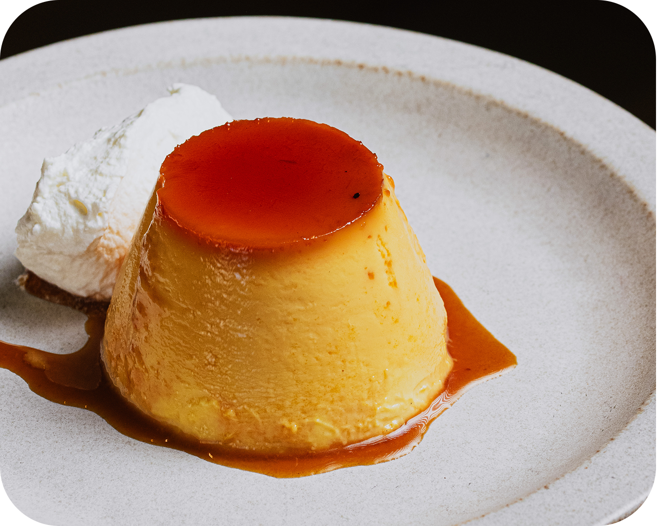 Flan con caramelo servido con una porción de crema batida en un plato blanco.