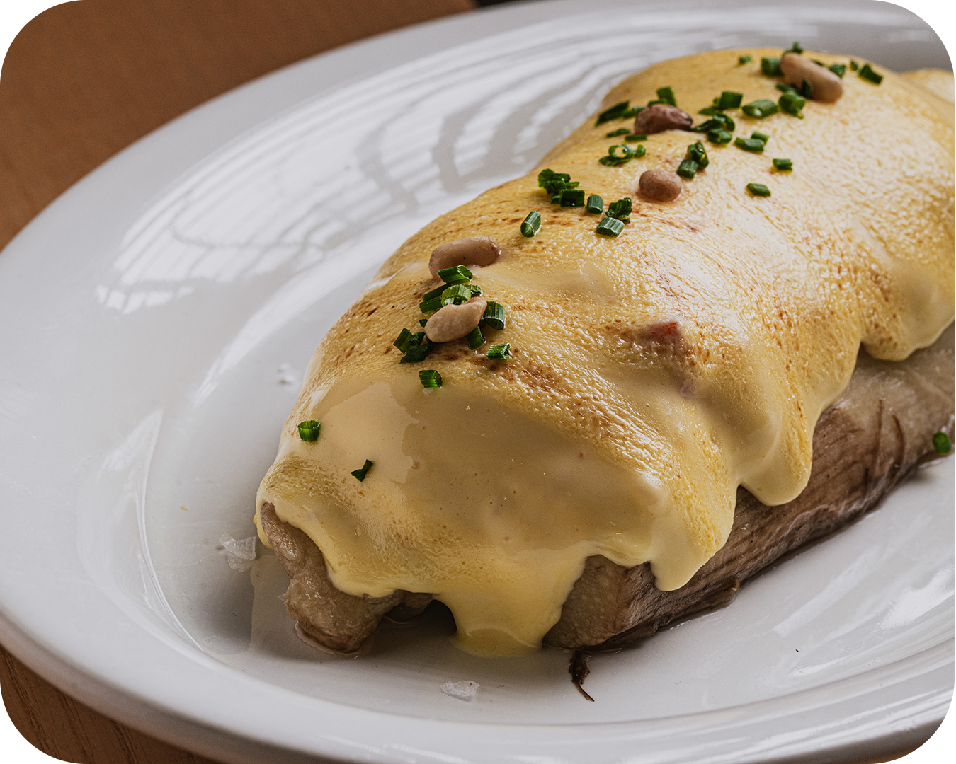 Bistec cubierto con huevo revuelto y queso, adornado con chives y cacahuates en un plato blanco.
