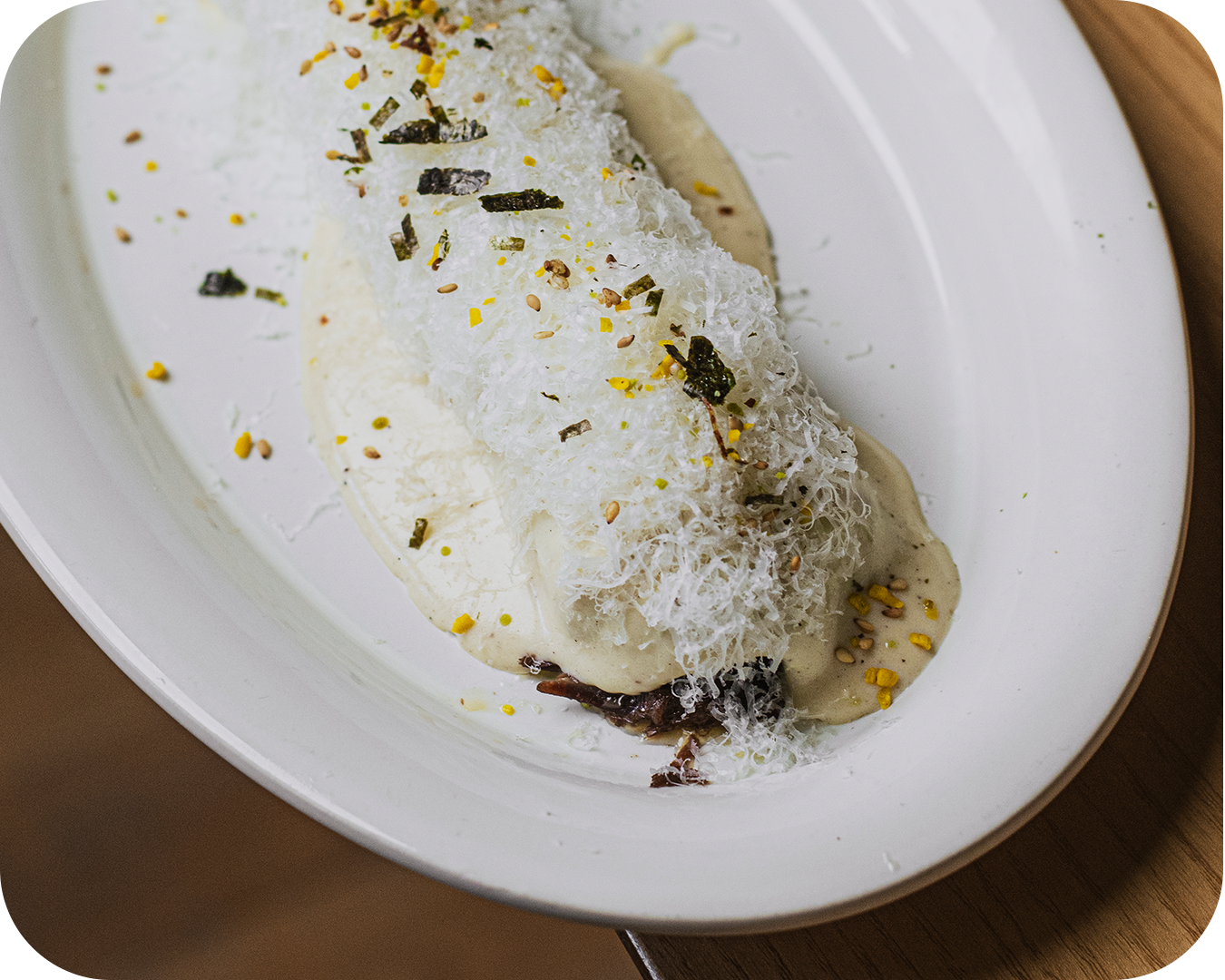 Plato de postre con crema, cabello de ángel, nueces, y escamas de queso en un plato blanco.