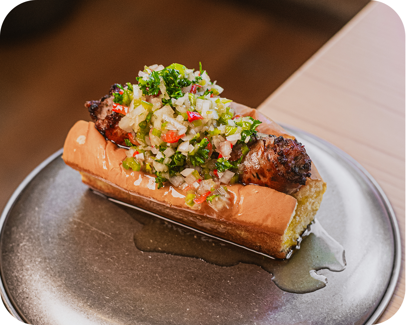 Perro caliente con salchicha, pan, y salsa, acompañado de un pico de gallo