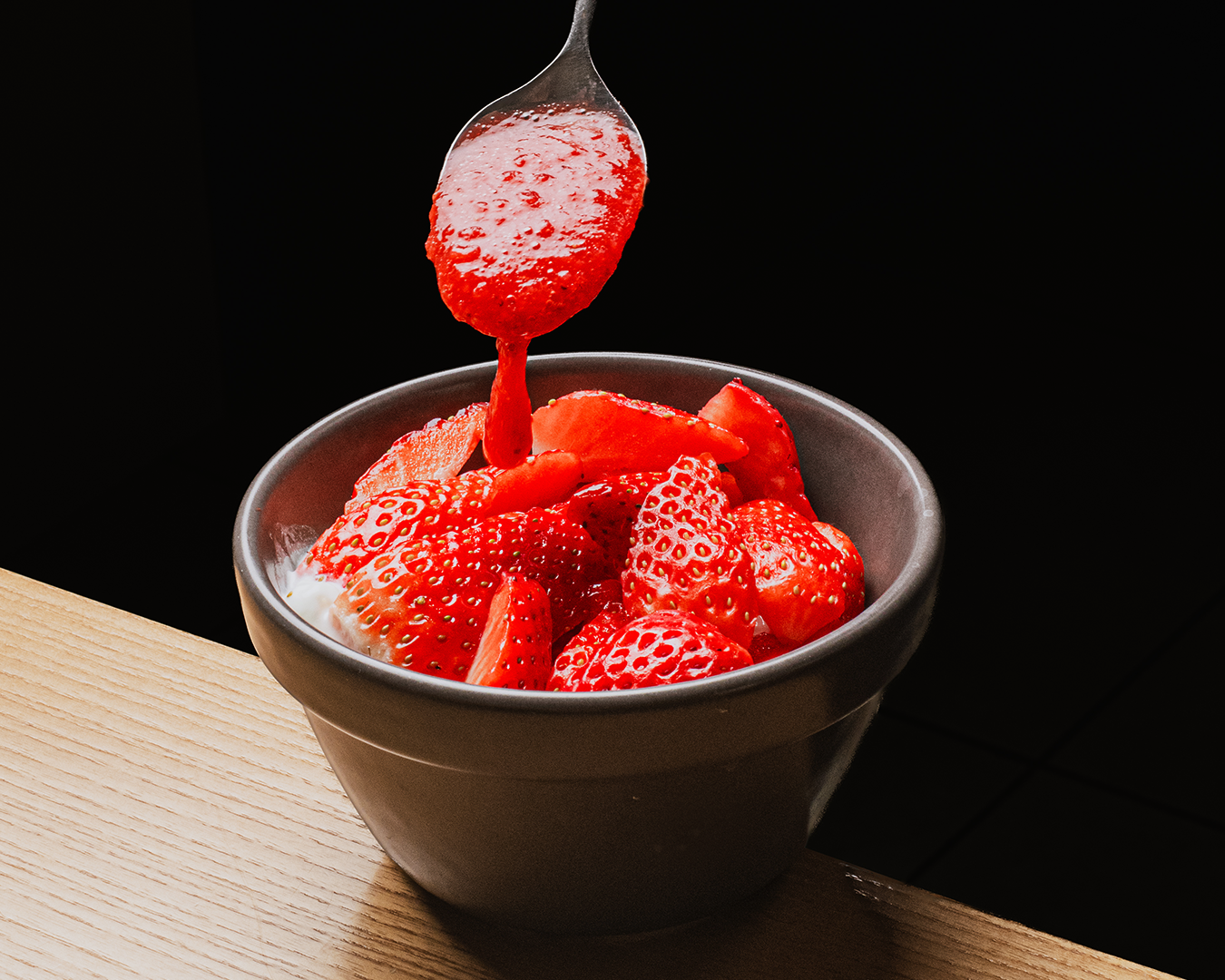 Fresas frescas en un tazón, con jarabe siendo vertido sobre ellas desde una cuchara