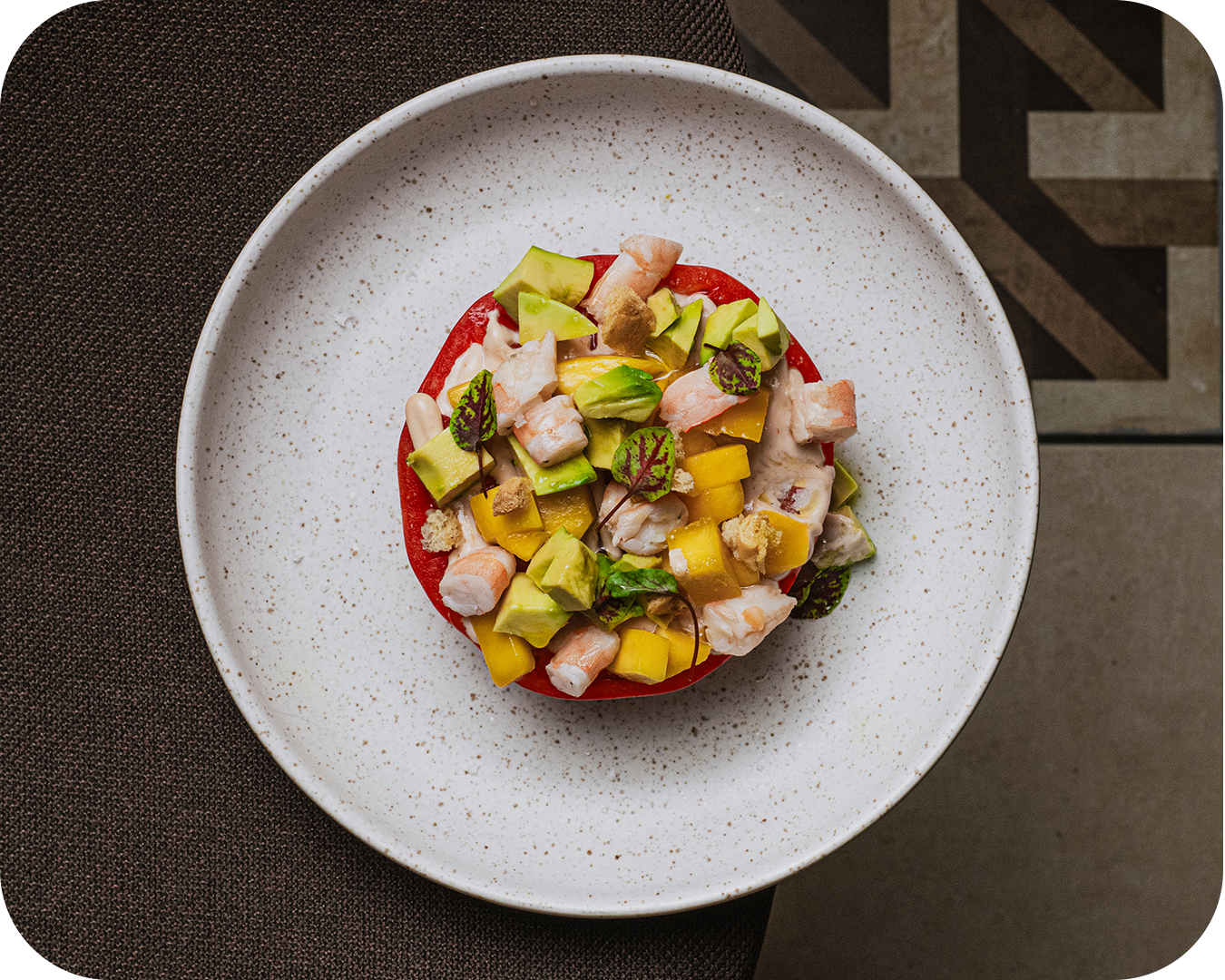 Ensalada con aguacate, mango, tomate y pollo en un plato blanco con fondo oscuro.