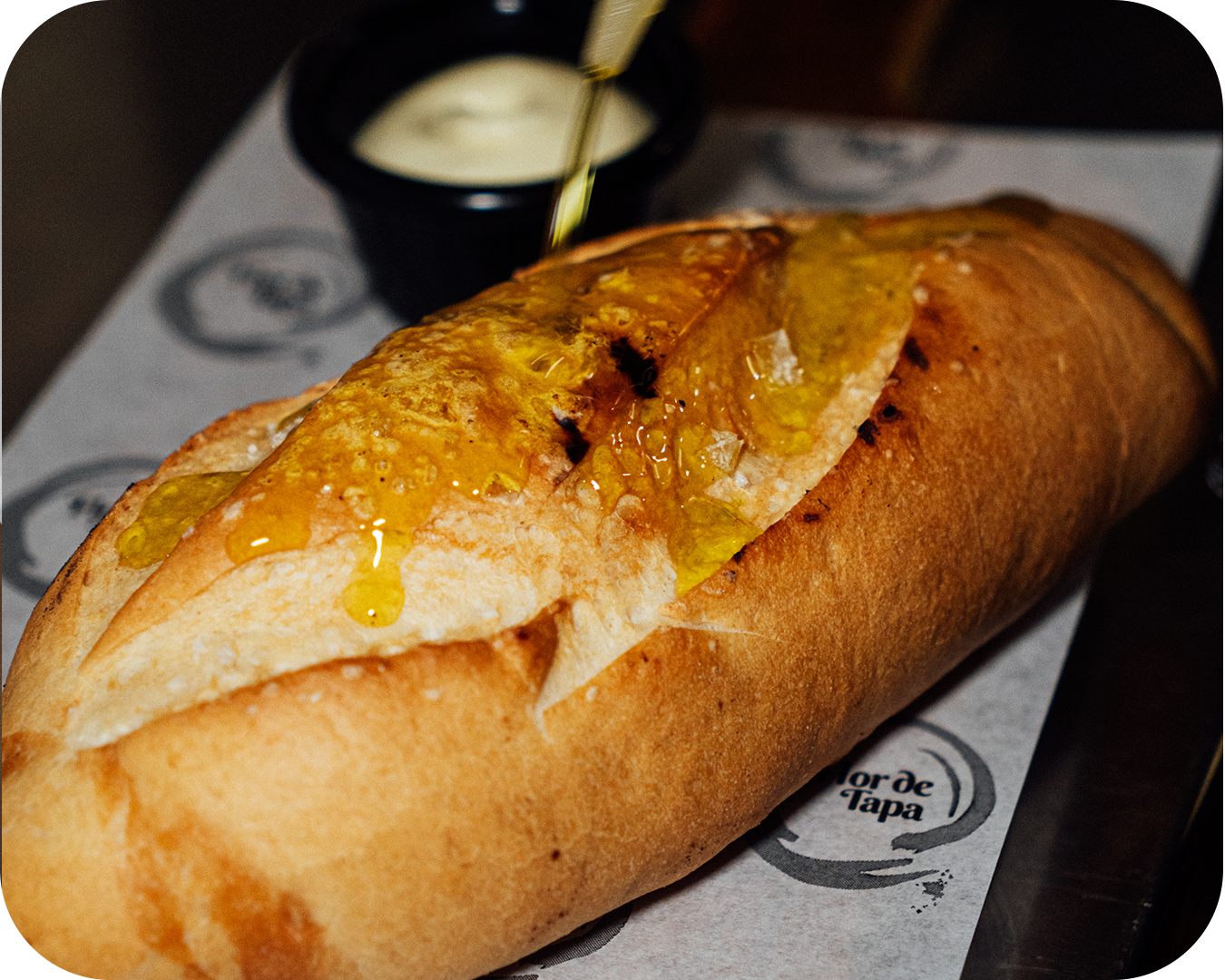 Baguette con mostaza y salsa en un plato de papel con el logotipo 'Torre de Tapas'.
